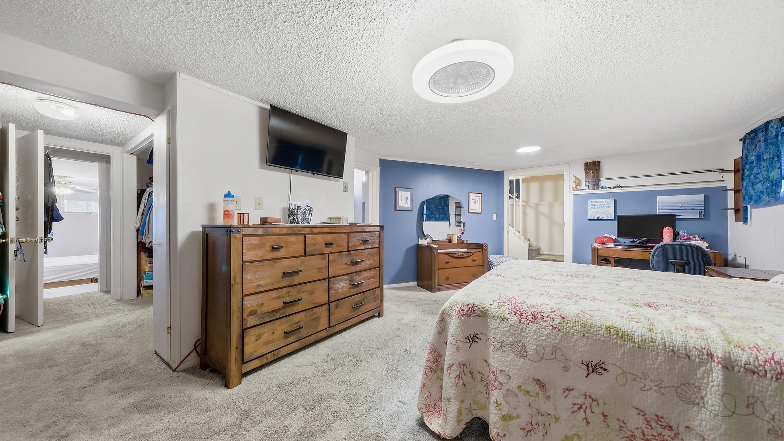 Bedroom with a coral-patterned quilt, blue accent walls, and wooden dressers.