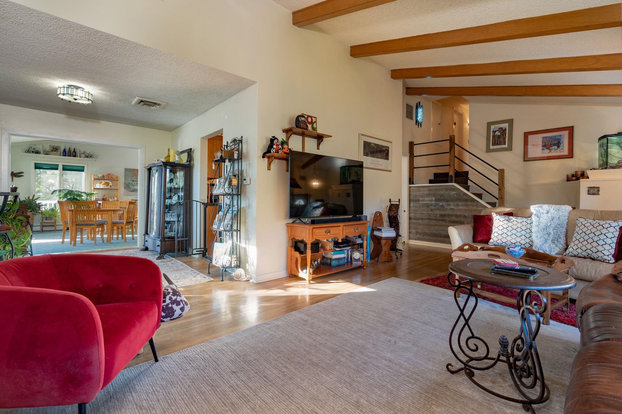 Living room with exposed wood beams, hardwood floors, and an open dining area.