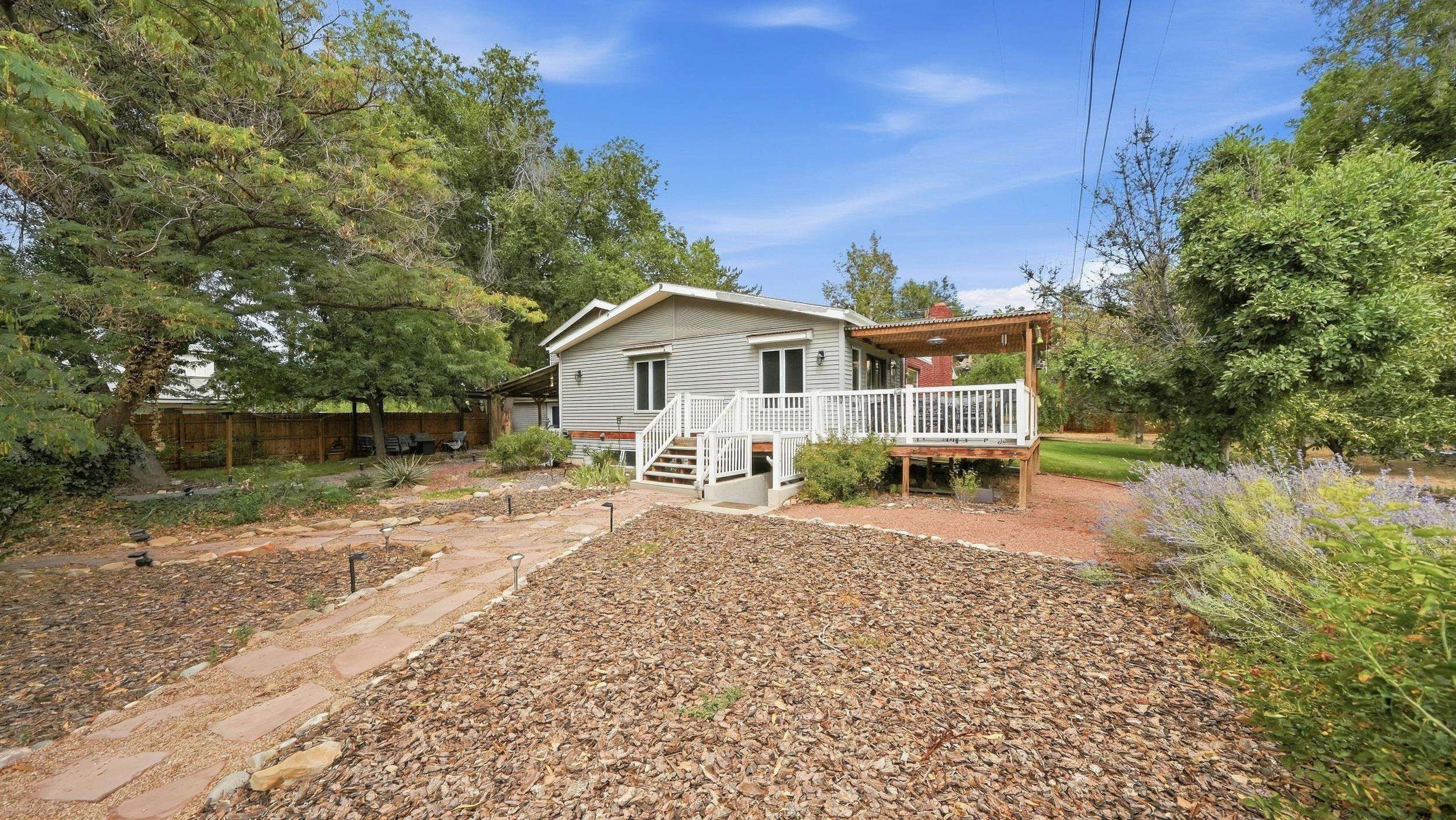 Light-colored home with a raised white-railed deck, pergola, and stone path through a landscaped yard.