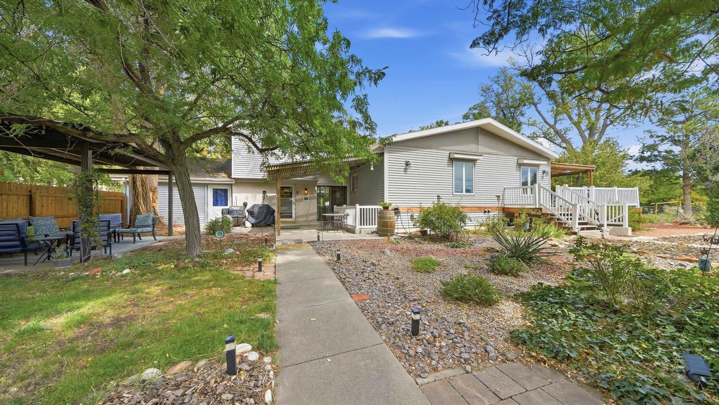 House exterior with a white-railed deck, shaded patio, and stone-landscaped walkway.