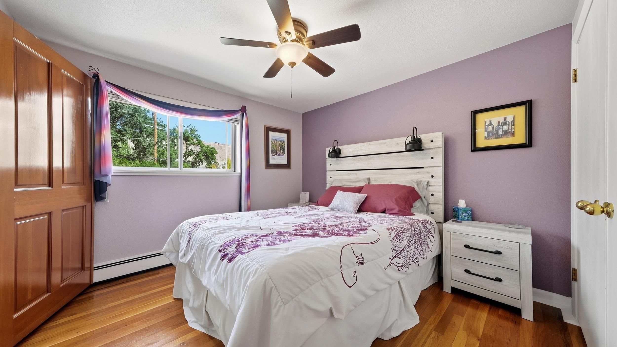 Bedroom with purple walls, patterned bedding, a white plank headboard, and a sunlit window.
