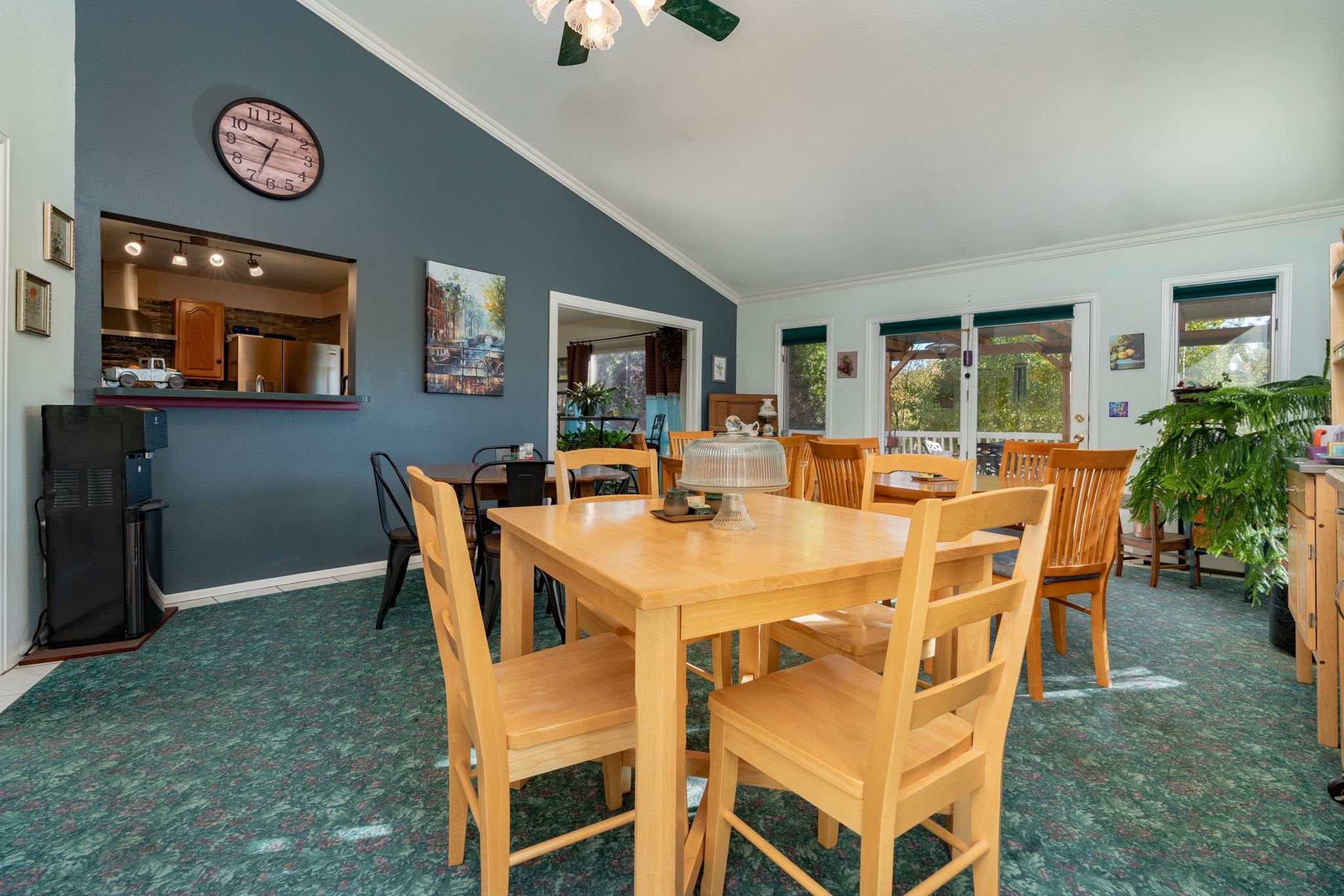 Dining room with a light-wood table, blue accent wall, kitchen pass-through, and glass doors to a covered patio.