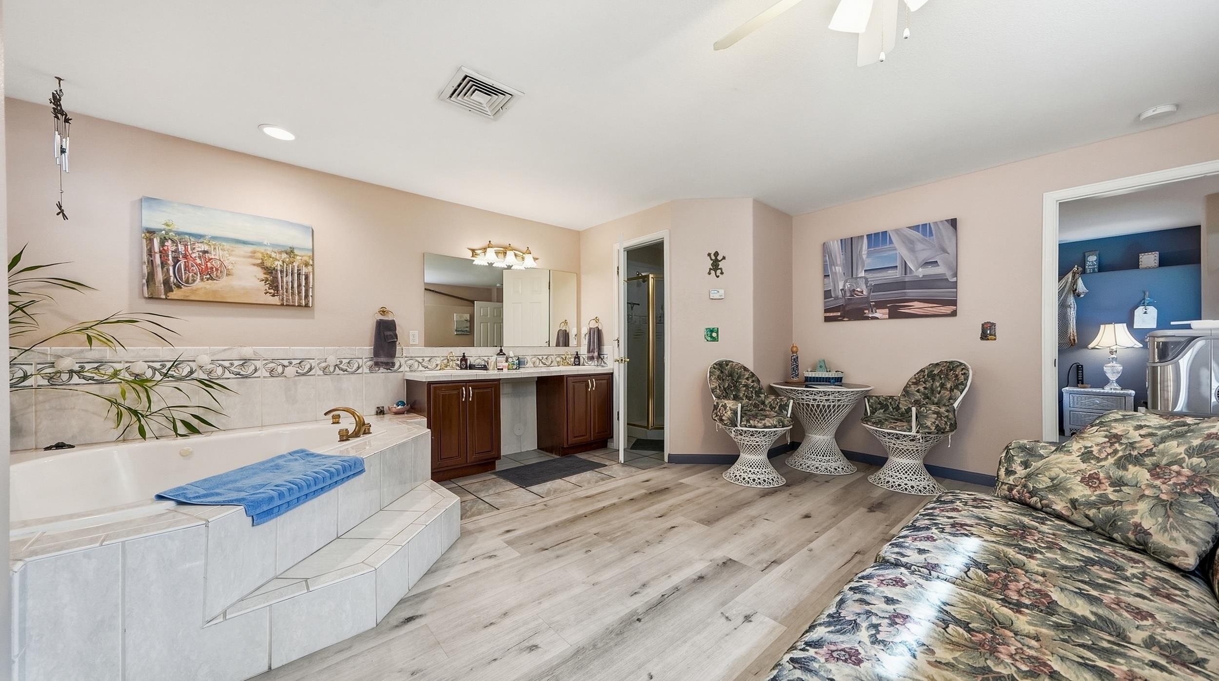 Spacious bathroom with a tiled soaking tub, dark wood vanity, and floral seating area.