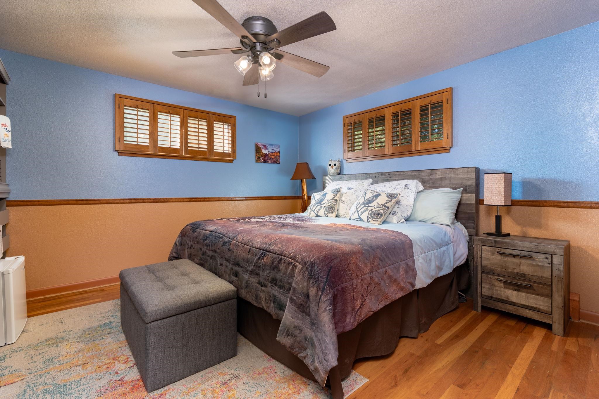 Furnished bedroom with wooden shutters, a ceiling fan, and a gray bench at the foot of the bed.