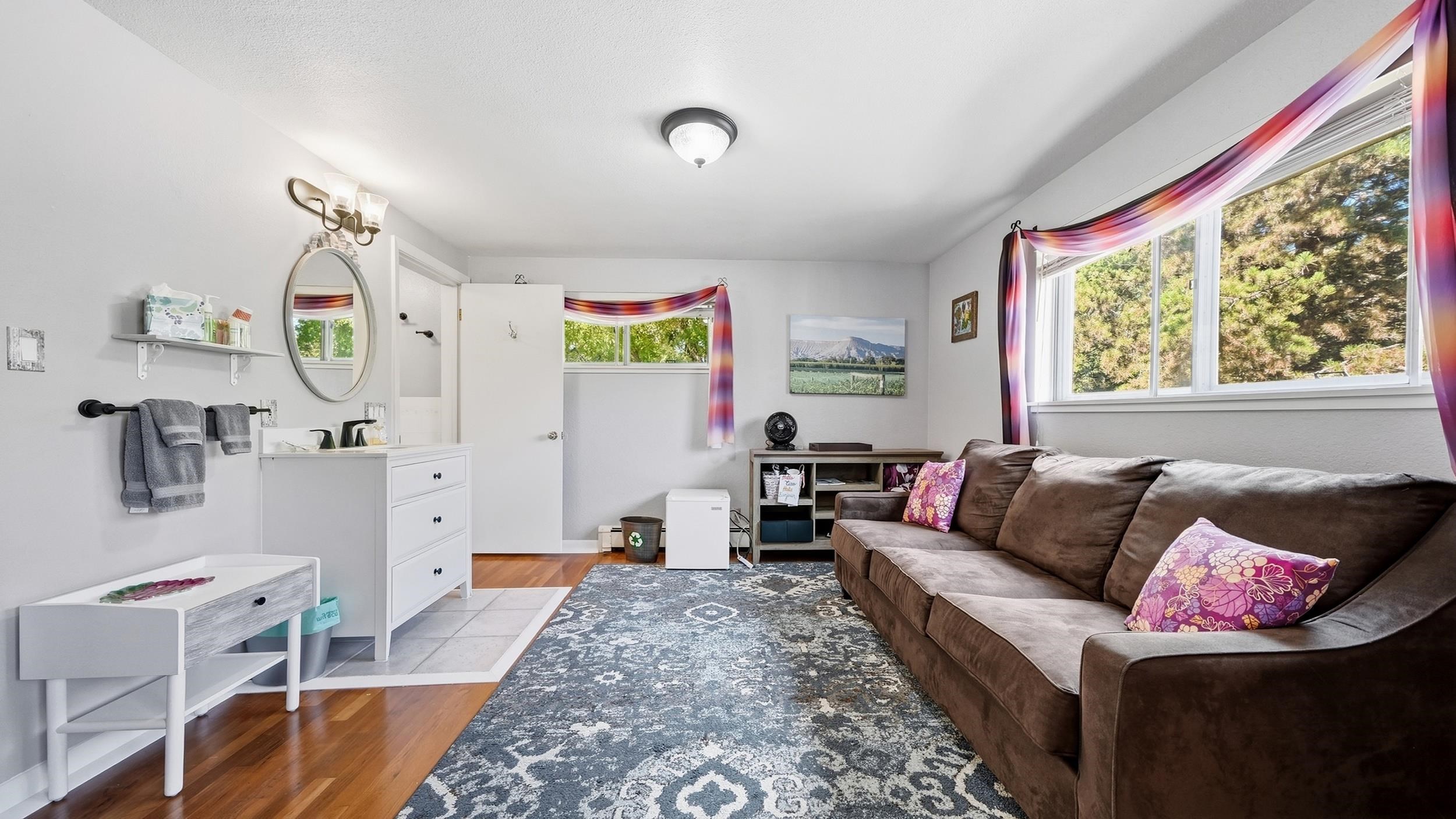 Furnished sitting room with brown sectional, patterned rug, vanity, and bright curtained windows.