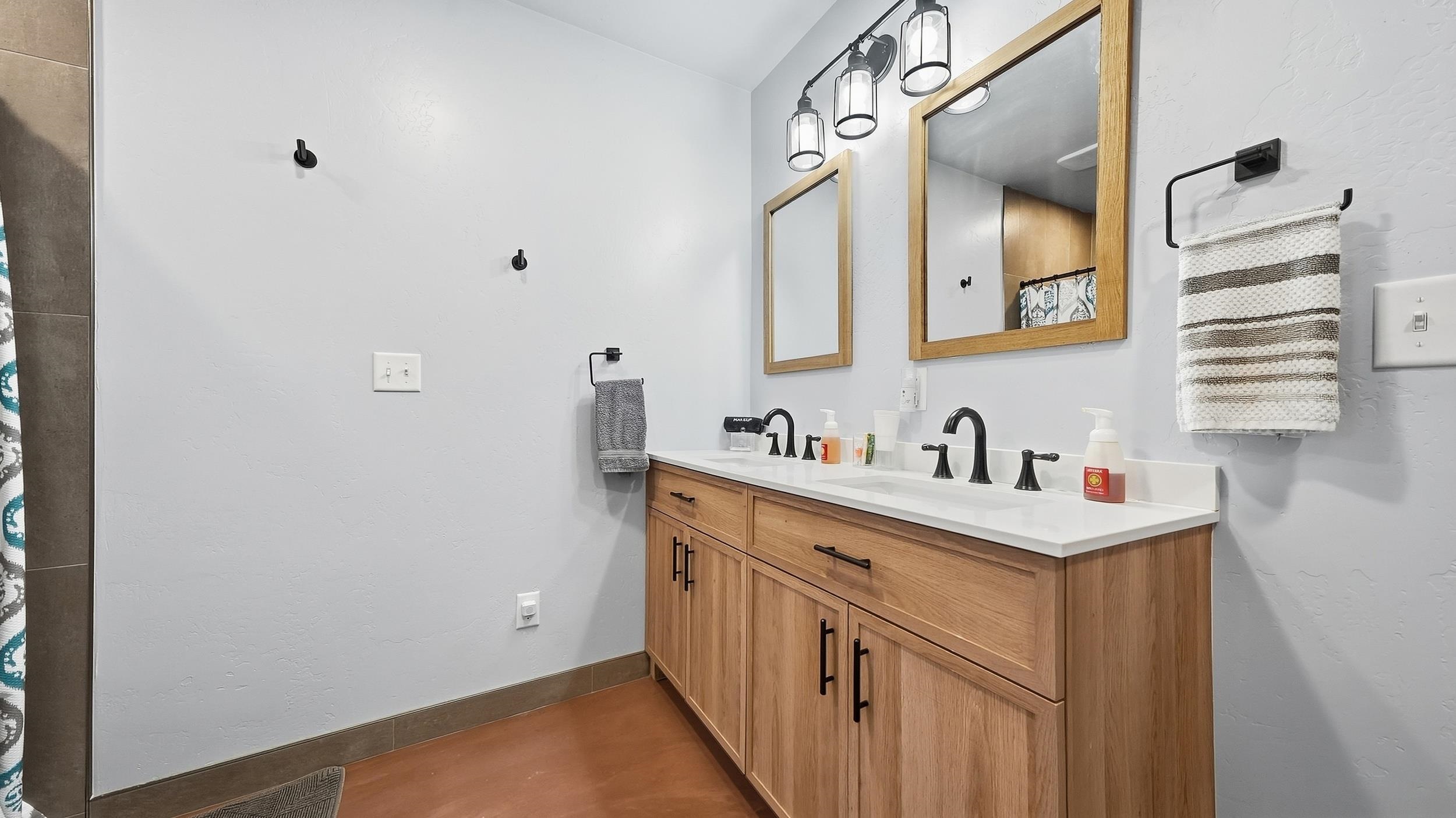 Bathroom with a light-wood double vanity, black faucets, wood-framed mirrors, and pendant lighting.
