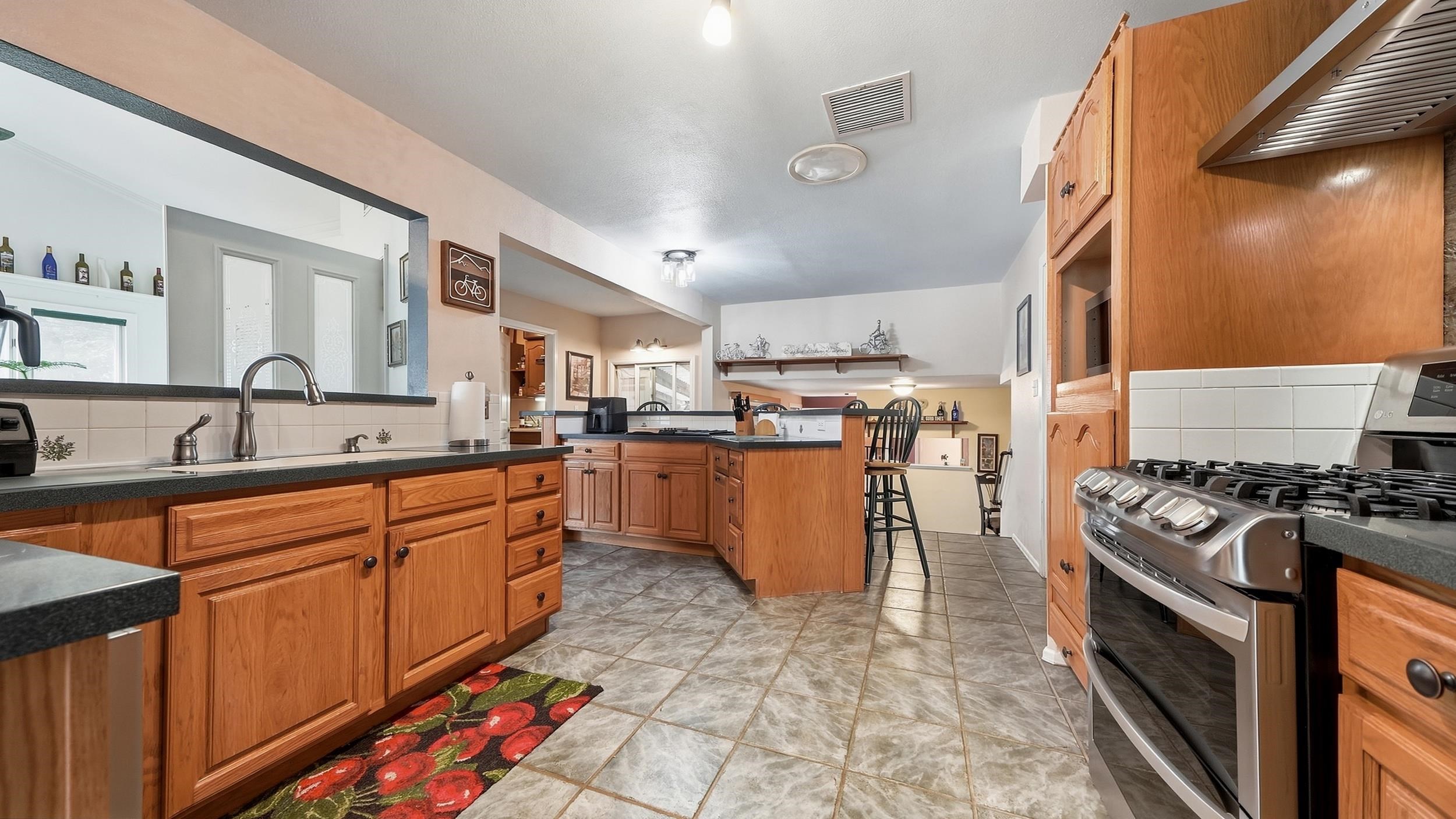 Kitchen with warm wood cabinets, tiled floors, stainless steel range, and a central island with bar seating.