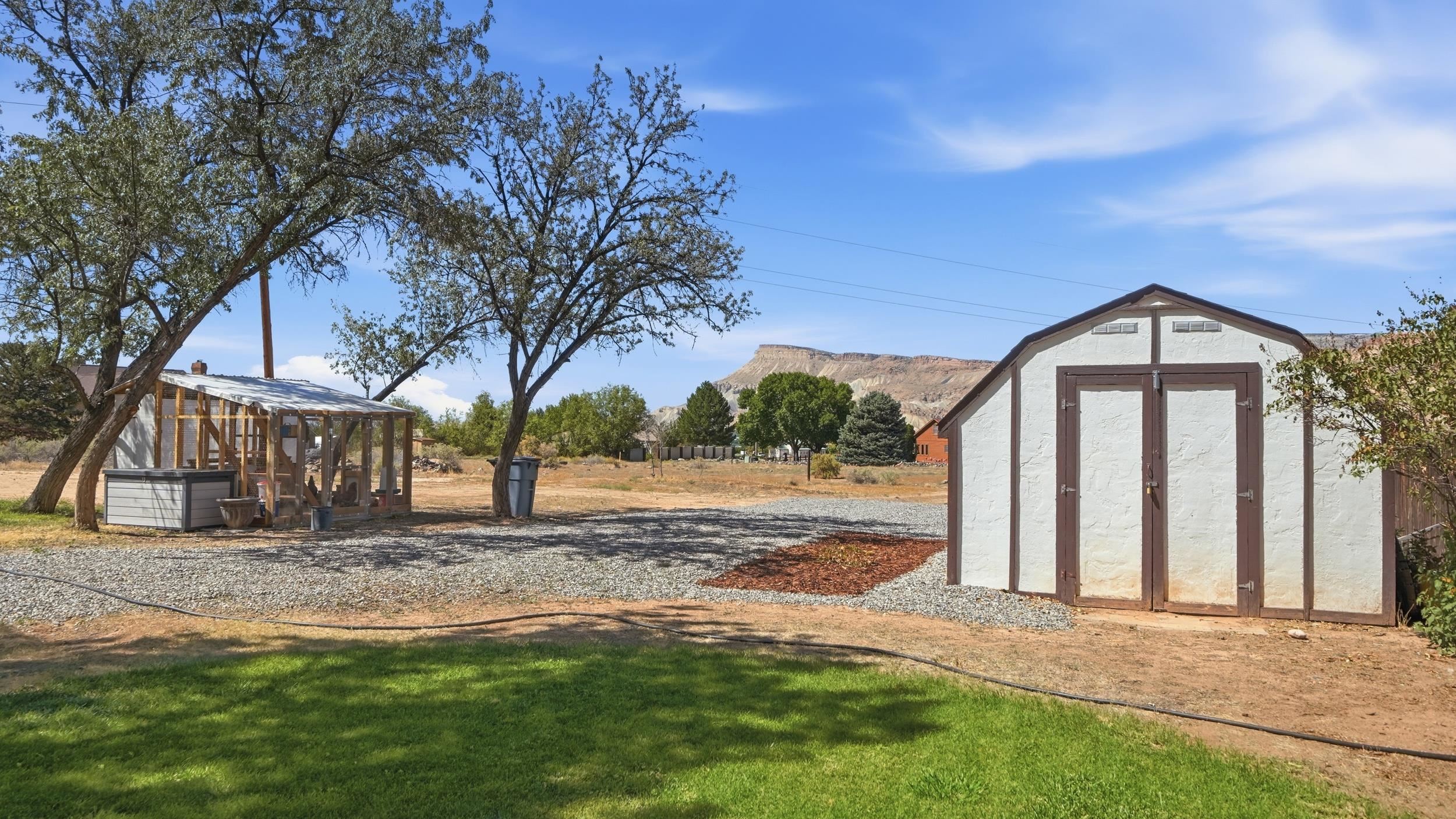 White storage shed and screened garden structure in a gravel yard, with a mesa in the distance.