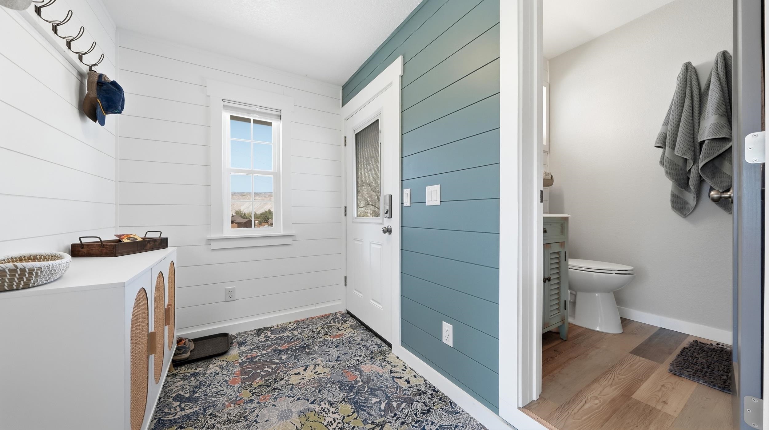 Entryway with blue shiplap accent wall, patterned rug, and adjoining bathroom.