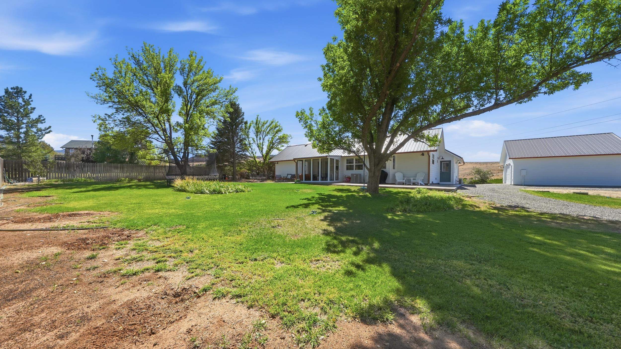 White home and detached outbuilding beyond a broad, tree-shaded lawn.