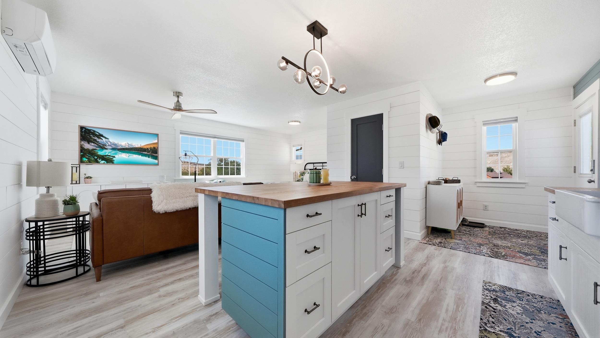Open-plan kitchen and living area with a blue island, wood countertop, and brown sofa.
