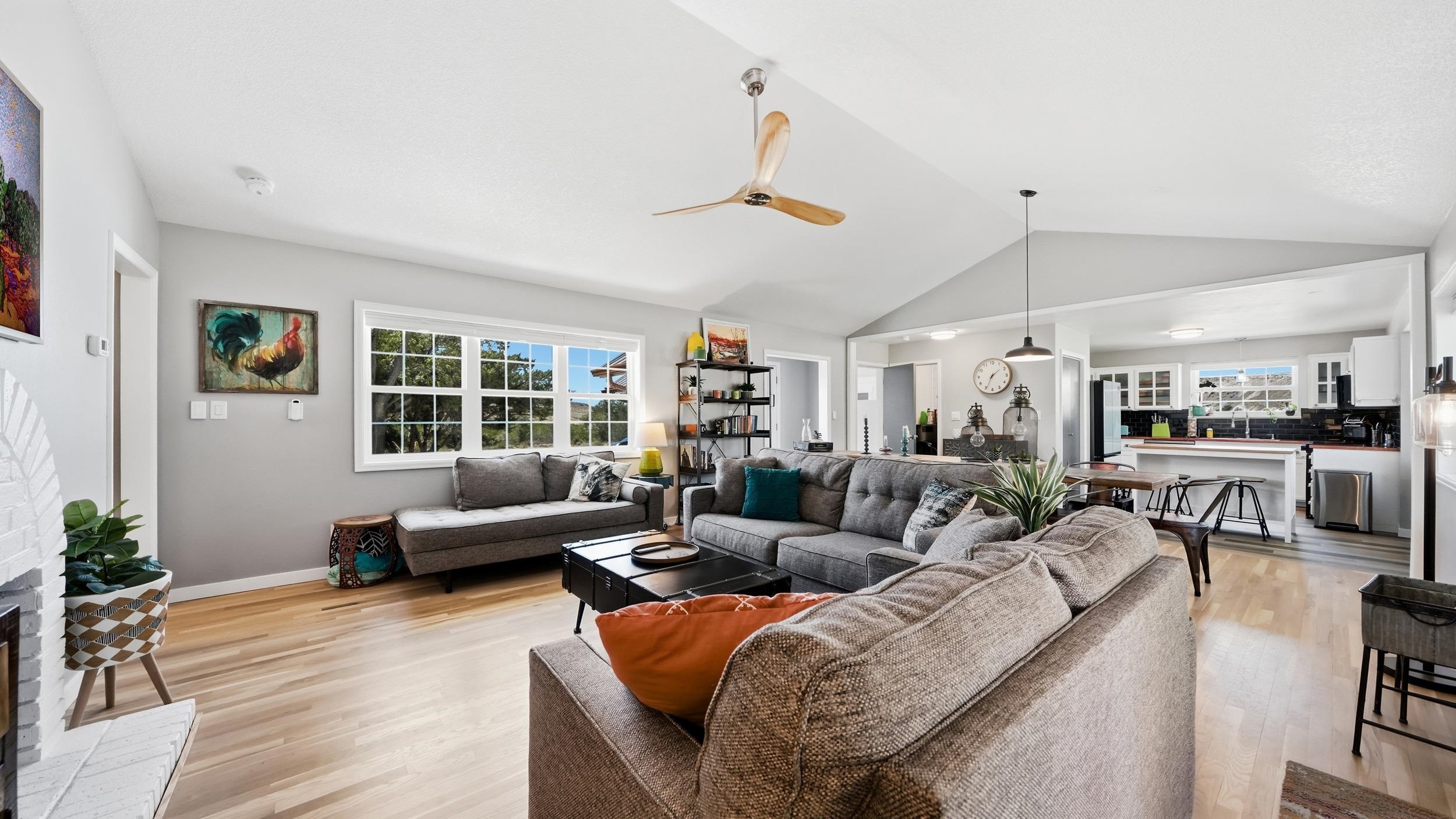 Open-plan living room with gray sofas, light wood floors, and a kitchen beyond.