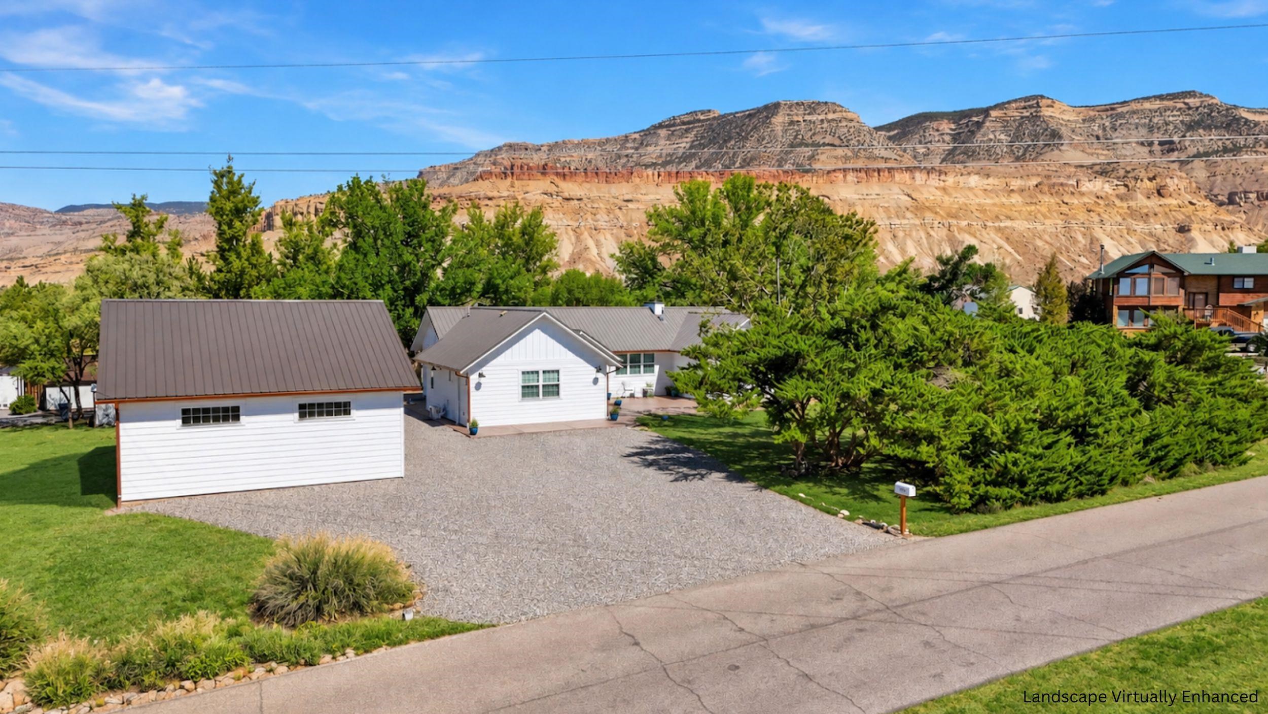 White home and detached garage with a gravel driveway beneath layered sandstone cliffs.