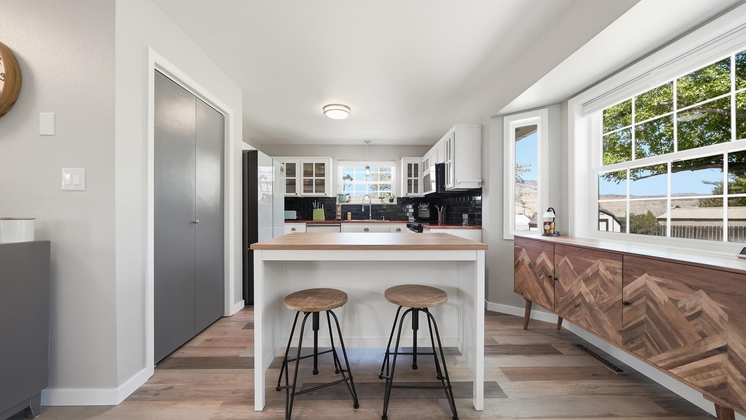 Bright kitchen with a wood-topped island, black tile backsplash, and large windows overlooking distant hills.