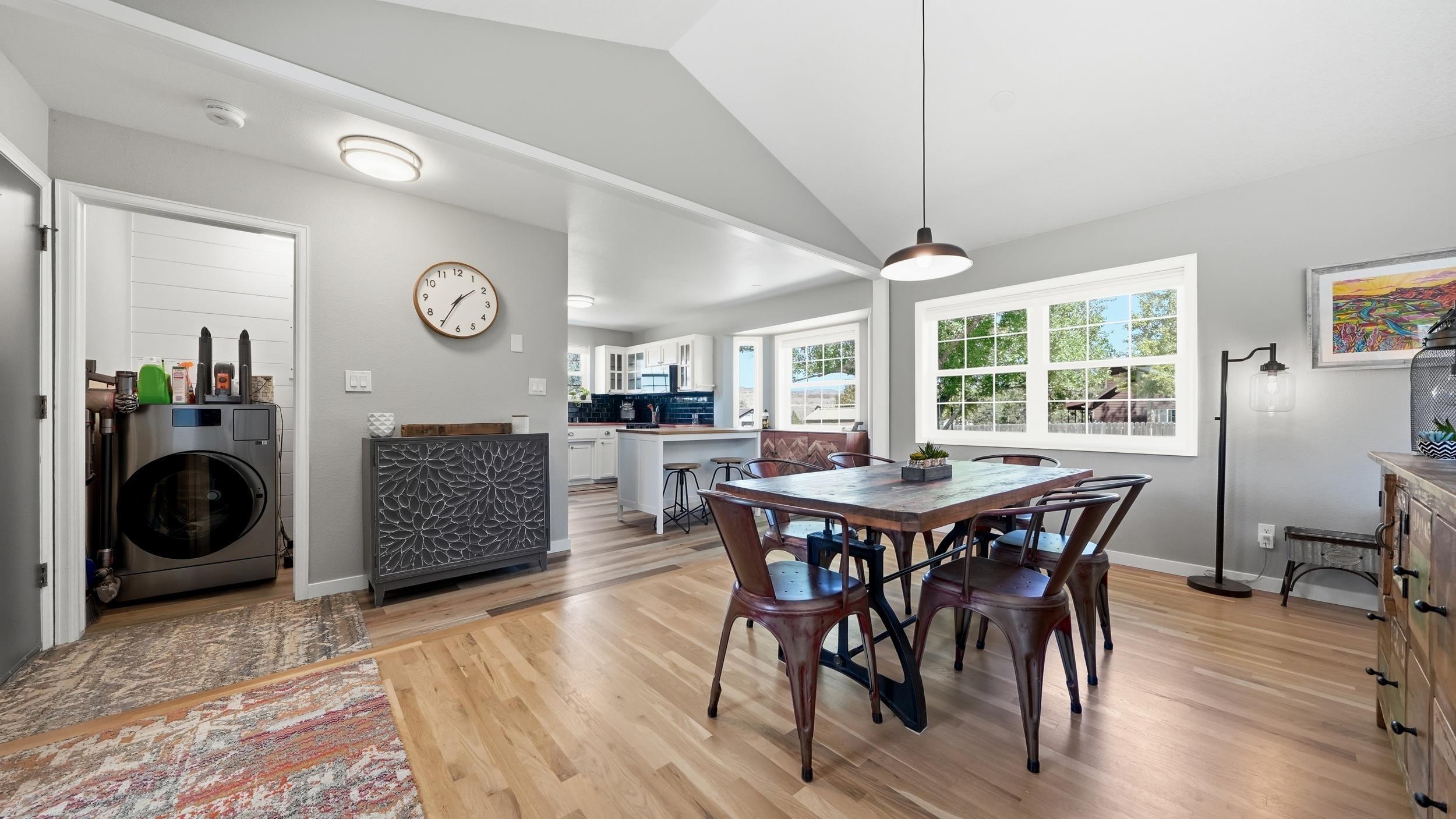 Open-plan dining room with a wood table and chairs beside a bright kitchen and laundry nook.