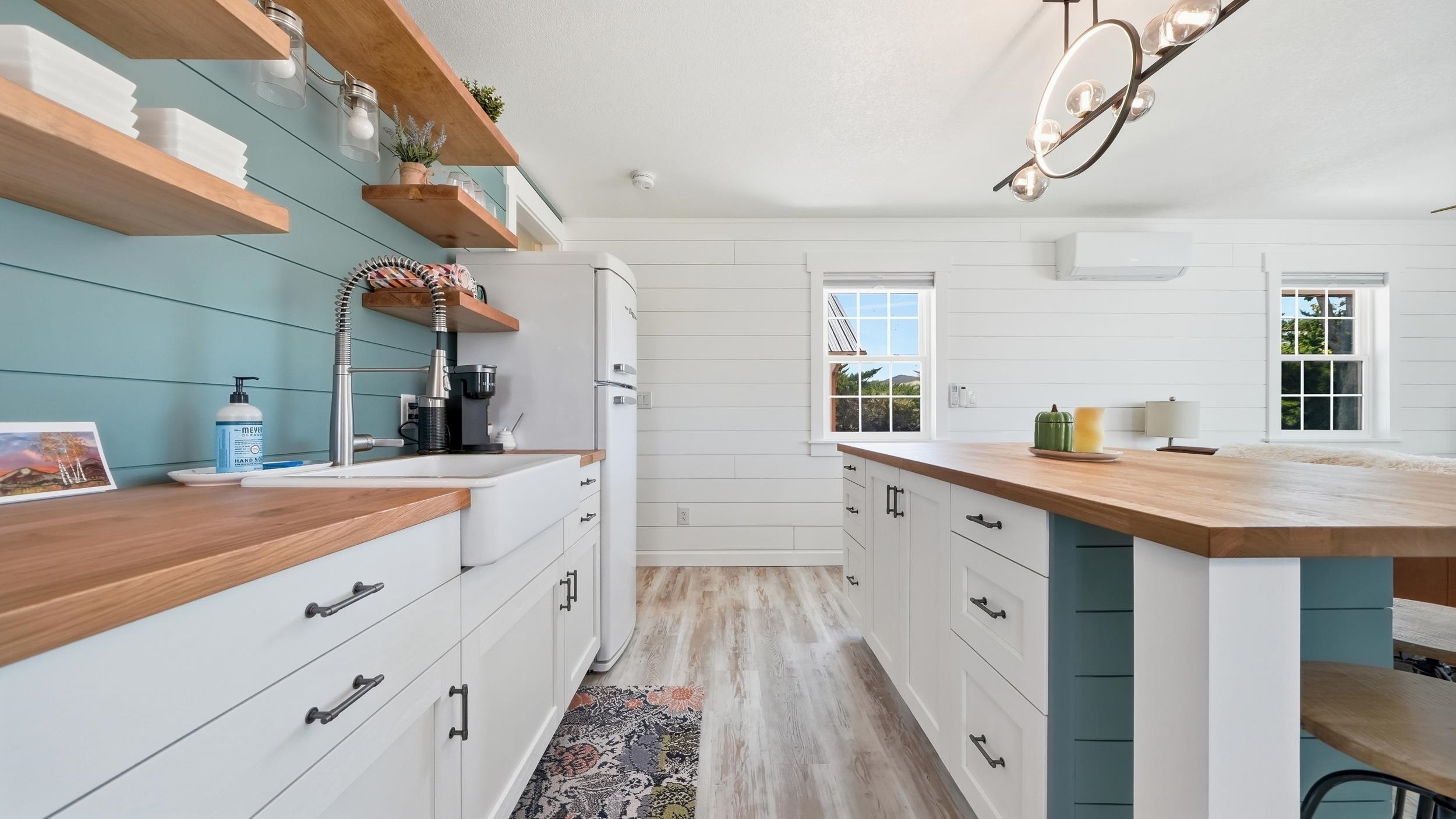 Bright kitchen with butcher-block counters, teal accent wall, open shelves, and a central island.