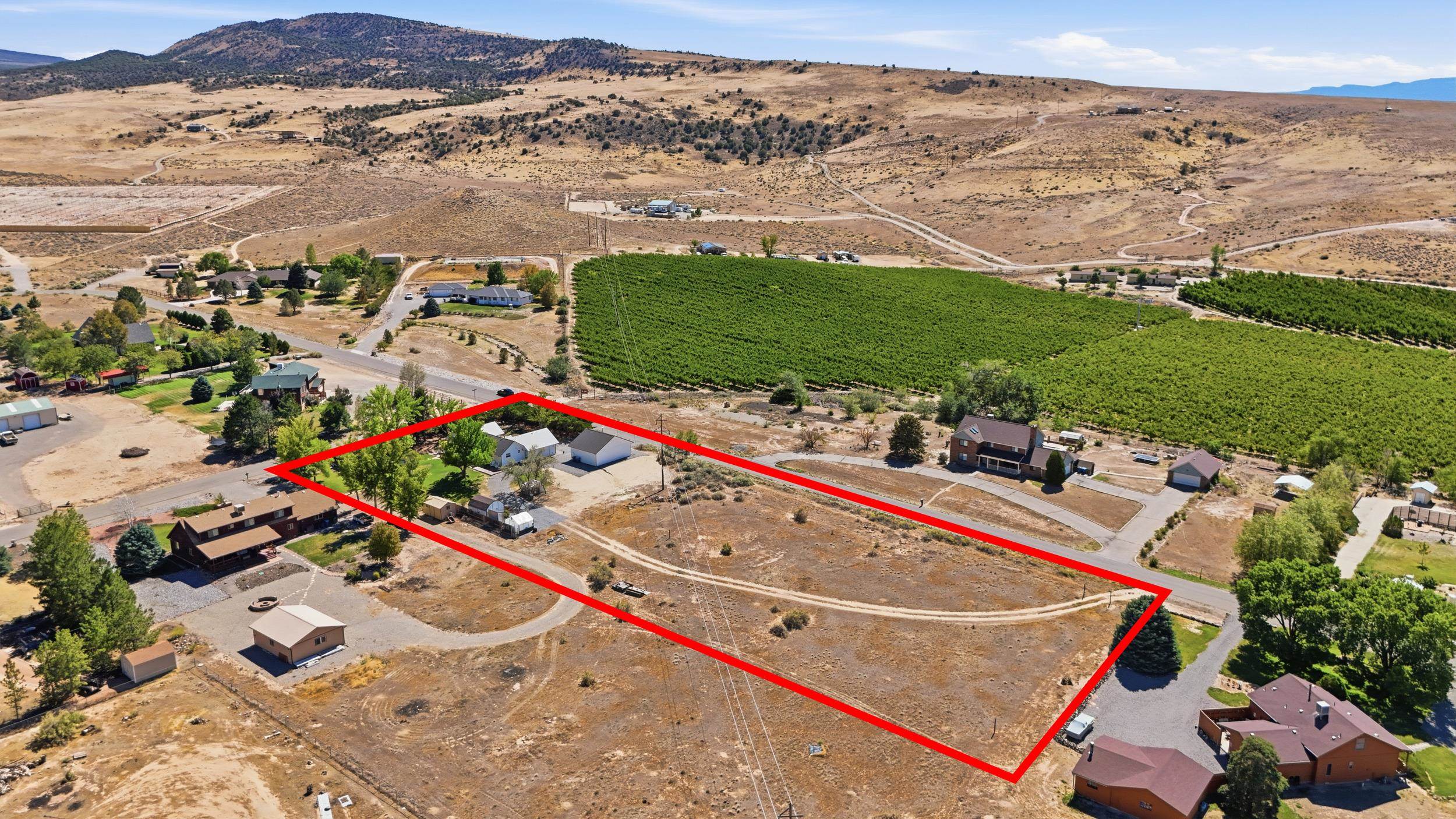 Aerial view of a dry parcel outlined in red, with buildings, an orchard, and mountains beyond.