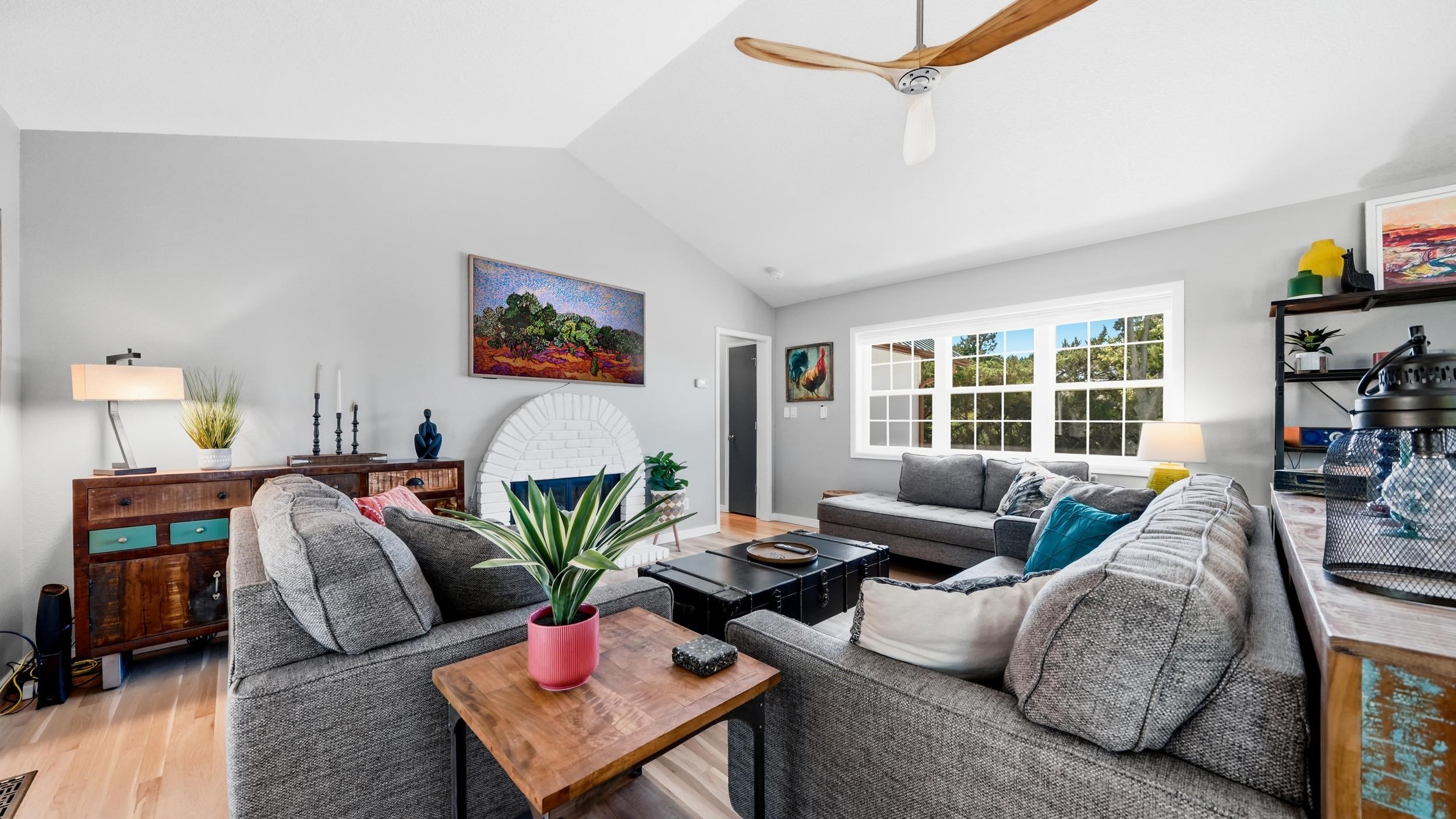 Furnished living room with gray sectionals, an arched white fireplace, and large divided-pane windows.