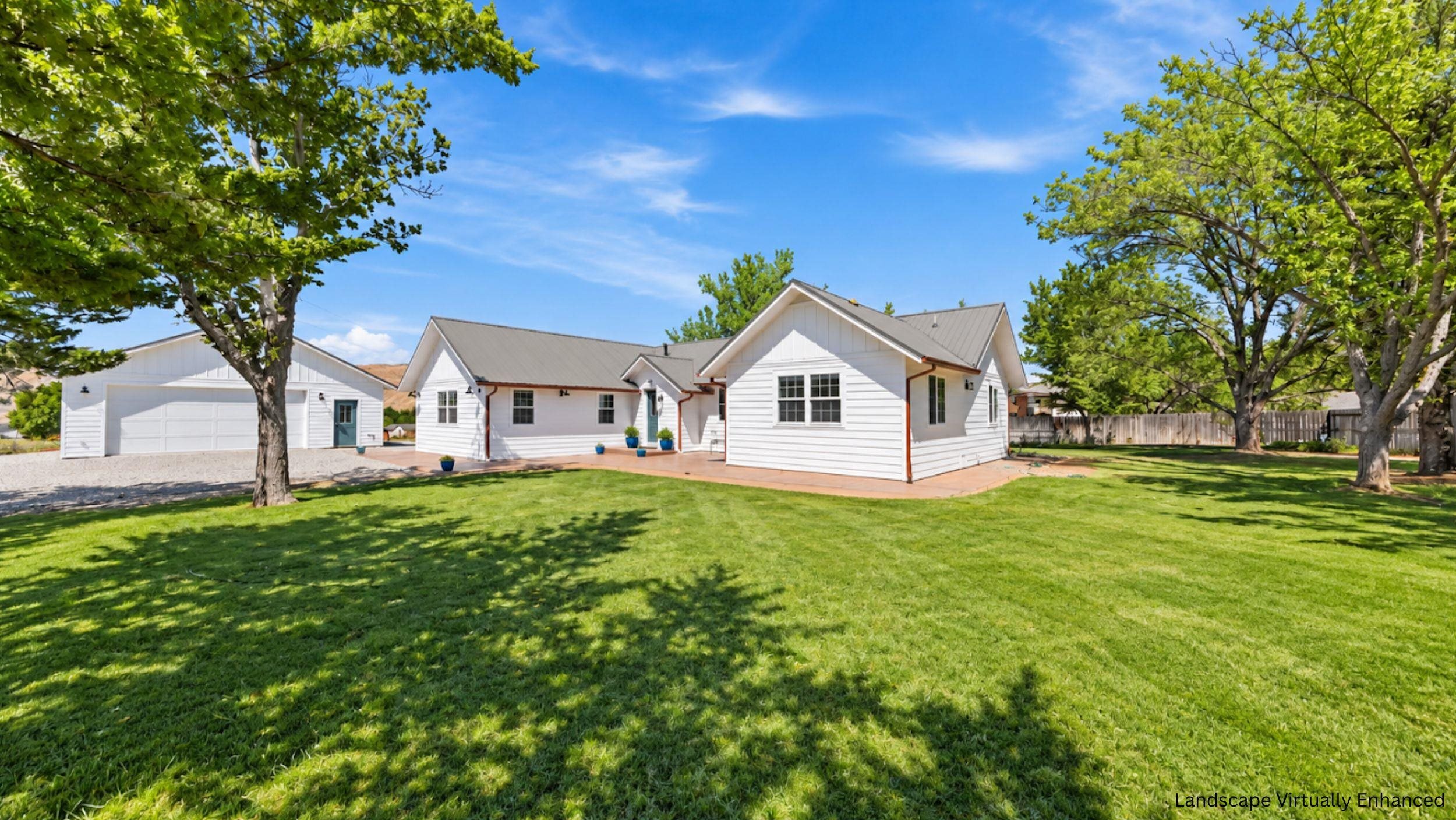White home with gray metal roofs and garage behind a tree-shaded lawn.