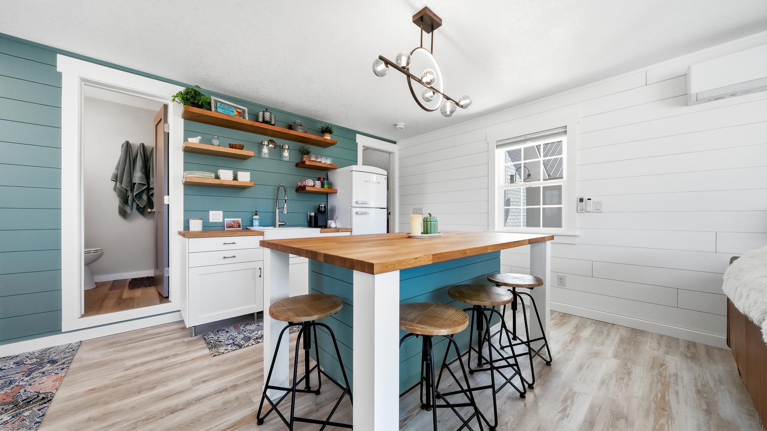 Kitchen with a teal island, wood countertop, floating shelves, and stools.