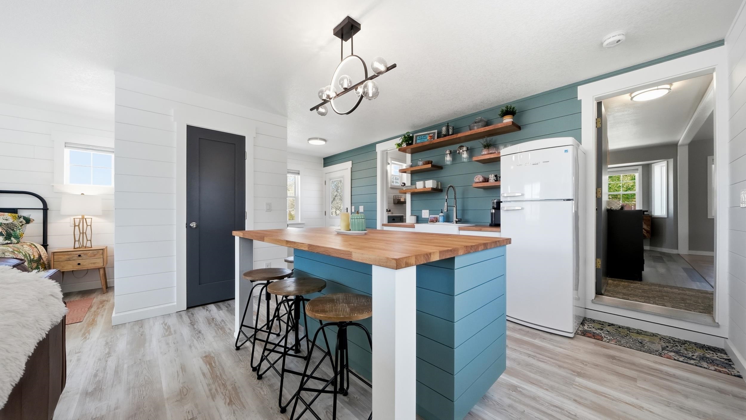 Kitchen with a teal island, butcher-block counter, floating shelves, and white retro-style refrigerator.