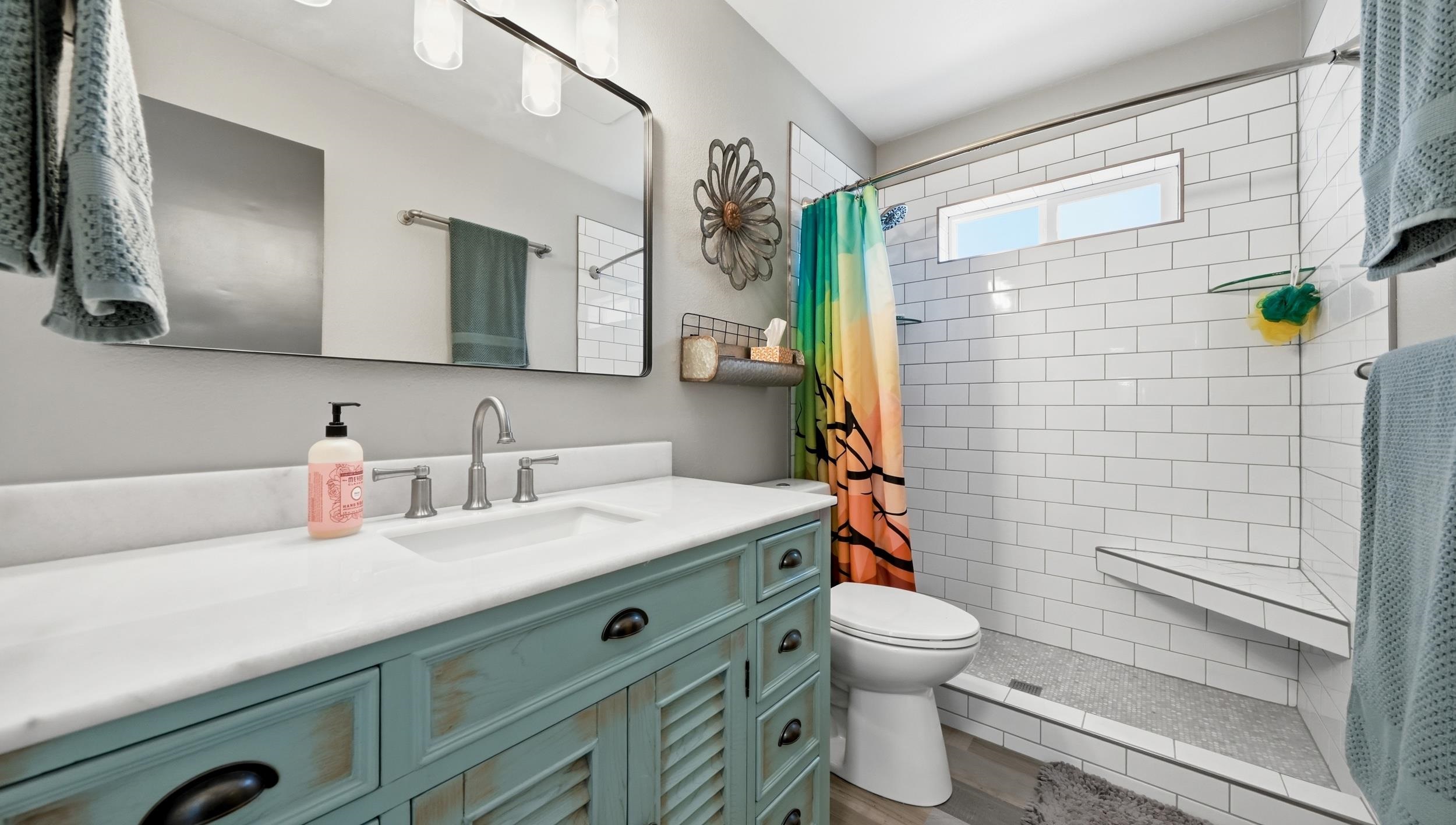 Bathroom with a distressed teal vanity and a white subway-tile shower with a colorful curtain.