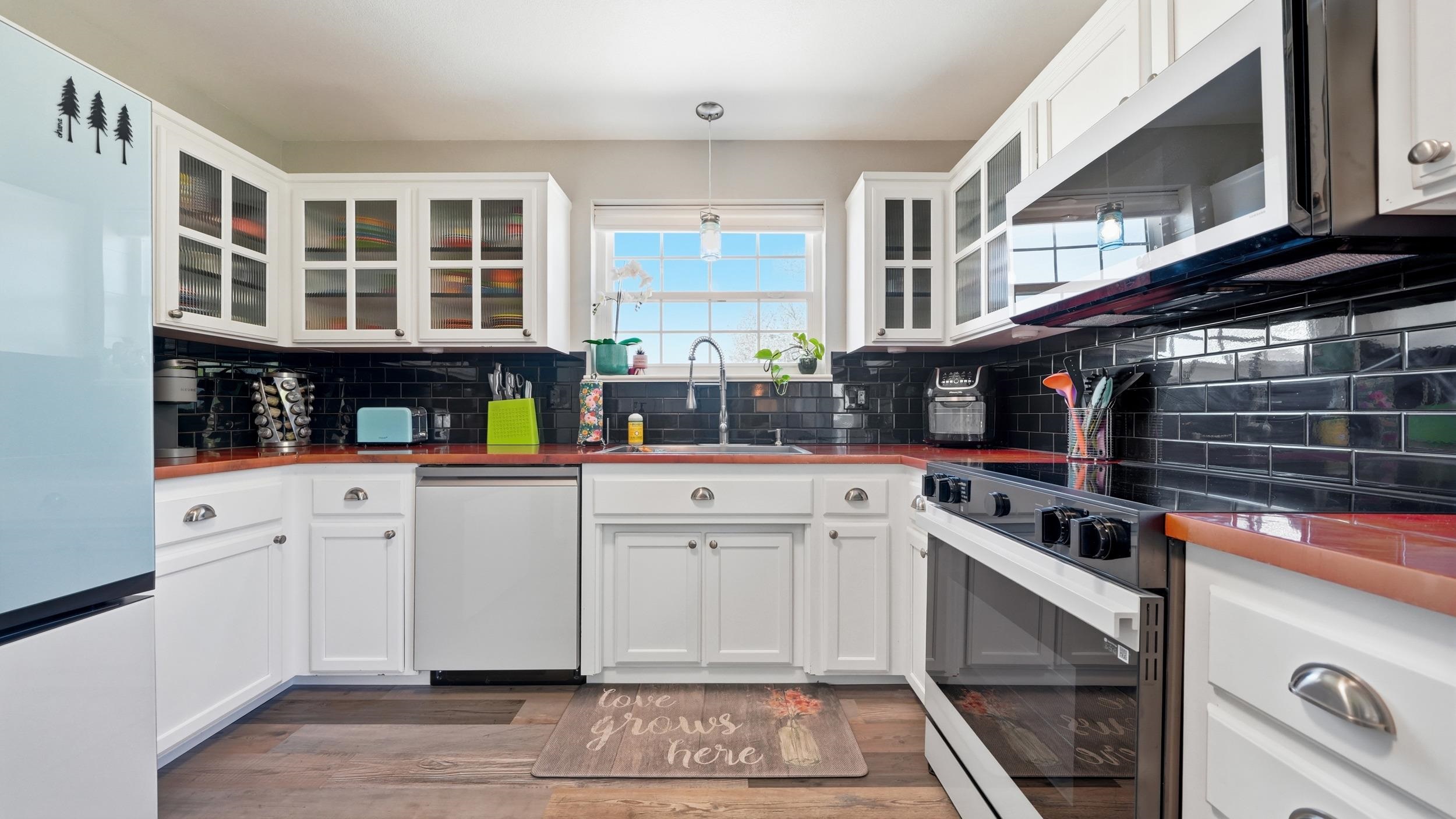 Kitchen with white cabinets, glossy black tile backsplash, and stainless-steel appliances.