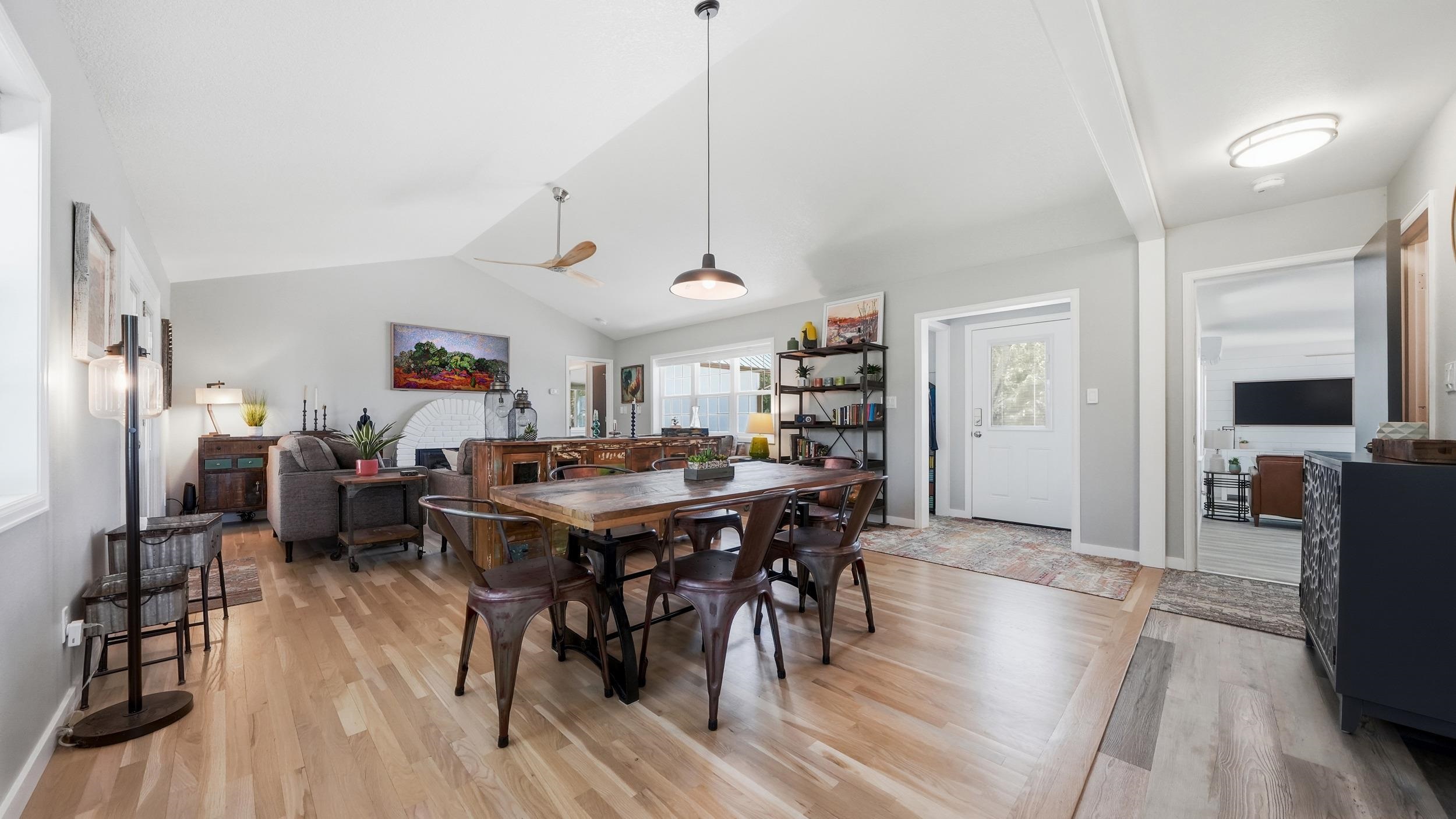 Open-plan dining and living room with a rustic wood table, hardwood floors, and white brick fireplace.