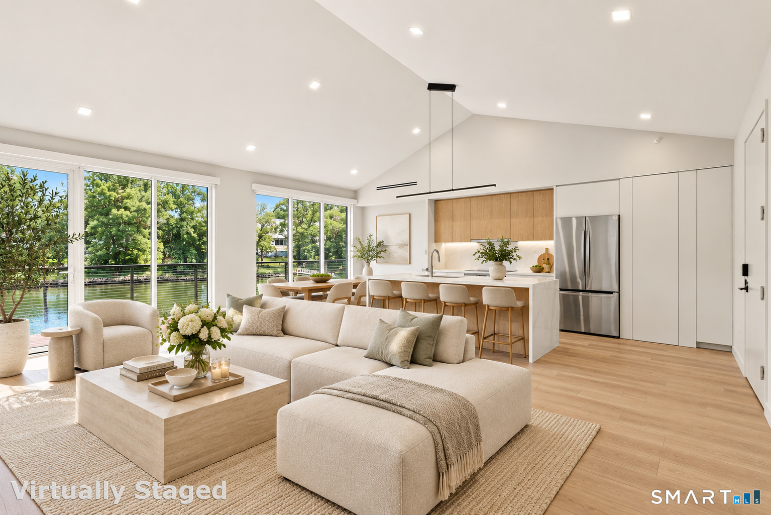 Open-plan living room and kitchen with a cream sectional and water views through large windows.