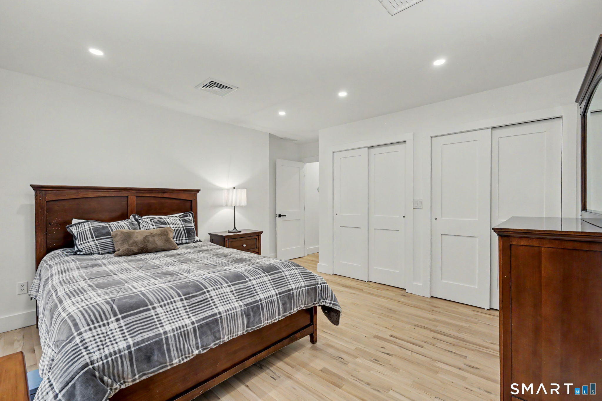 Bedroom with a dark wood bed, gray plaid bedding, white paneled doors, and light wood floors.