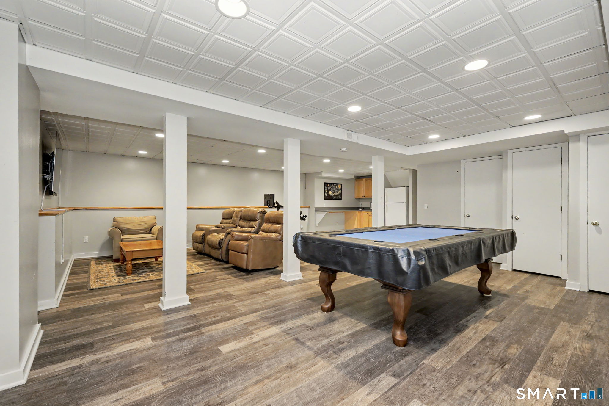 Finished basement game room with a pool table, leather seating, and a kitchenette.