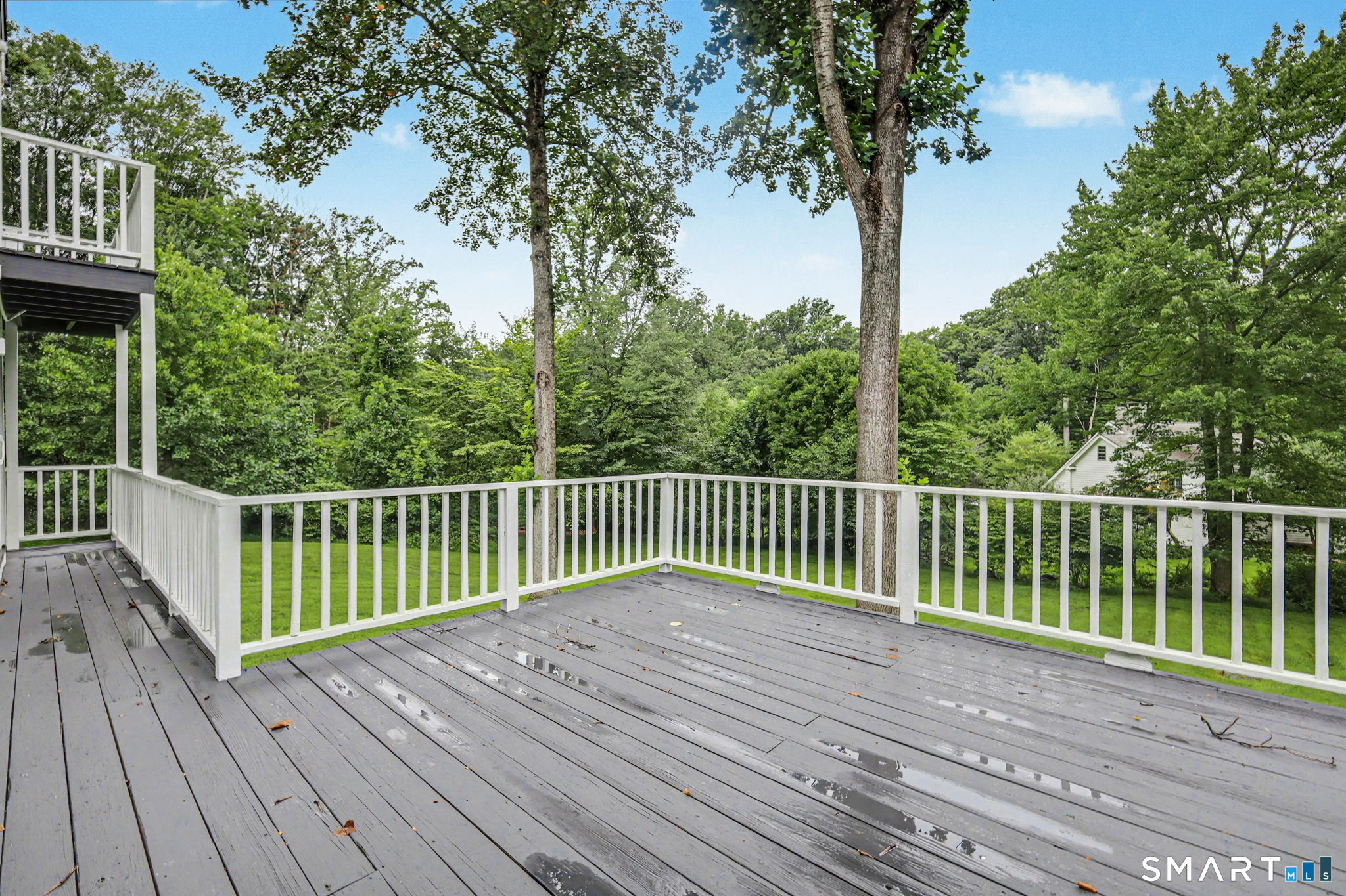 Spacious gray deck with white railings overlooking a wooded lawn.