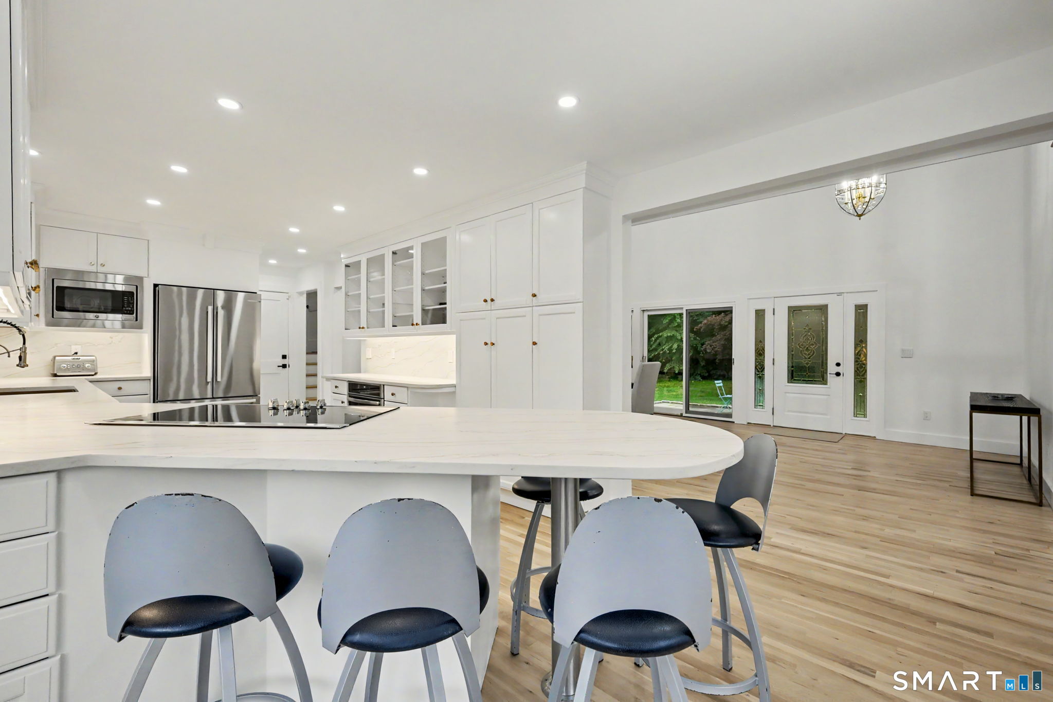 Bright white kitchen with a large cooktop island, gray bar stools, and glass doors to the yard.