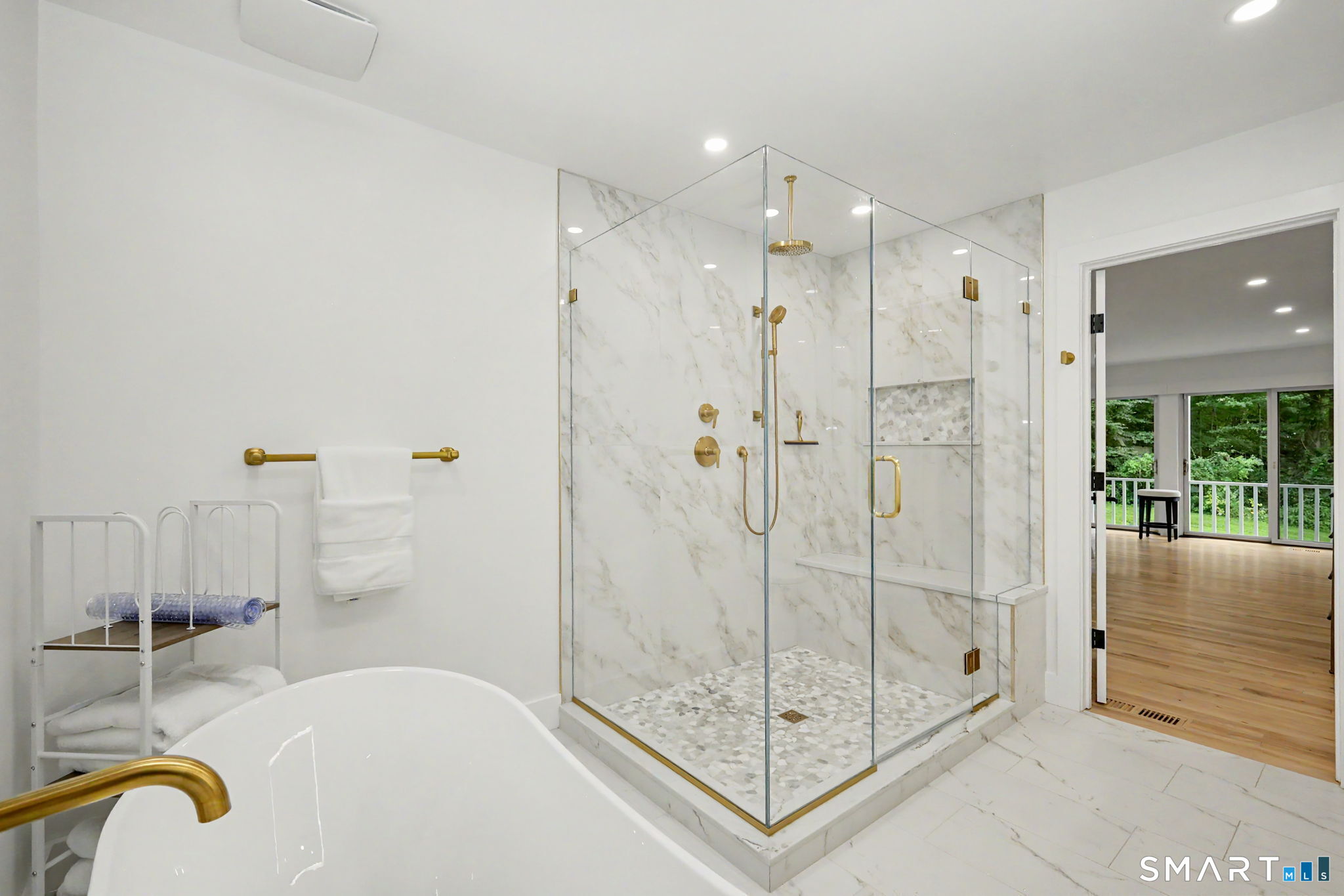 Marble bathroom with a freestanding tub and glass shower featuring gold fixtures.