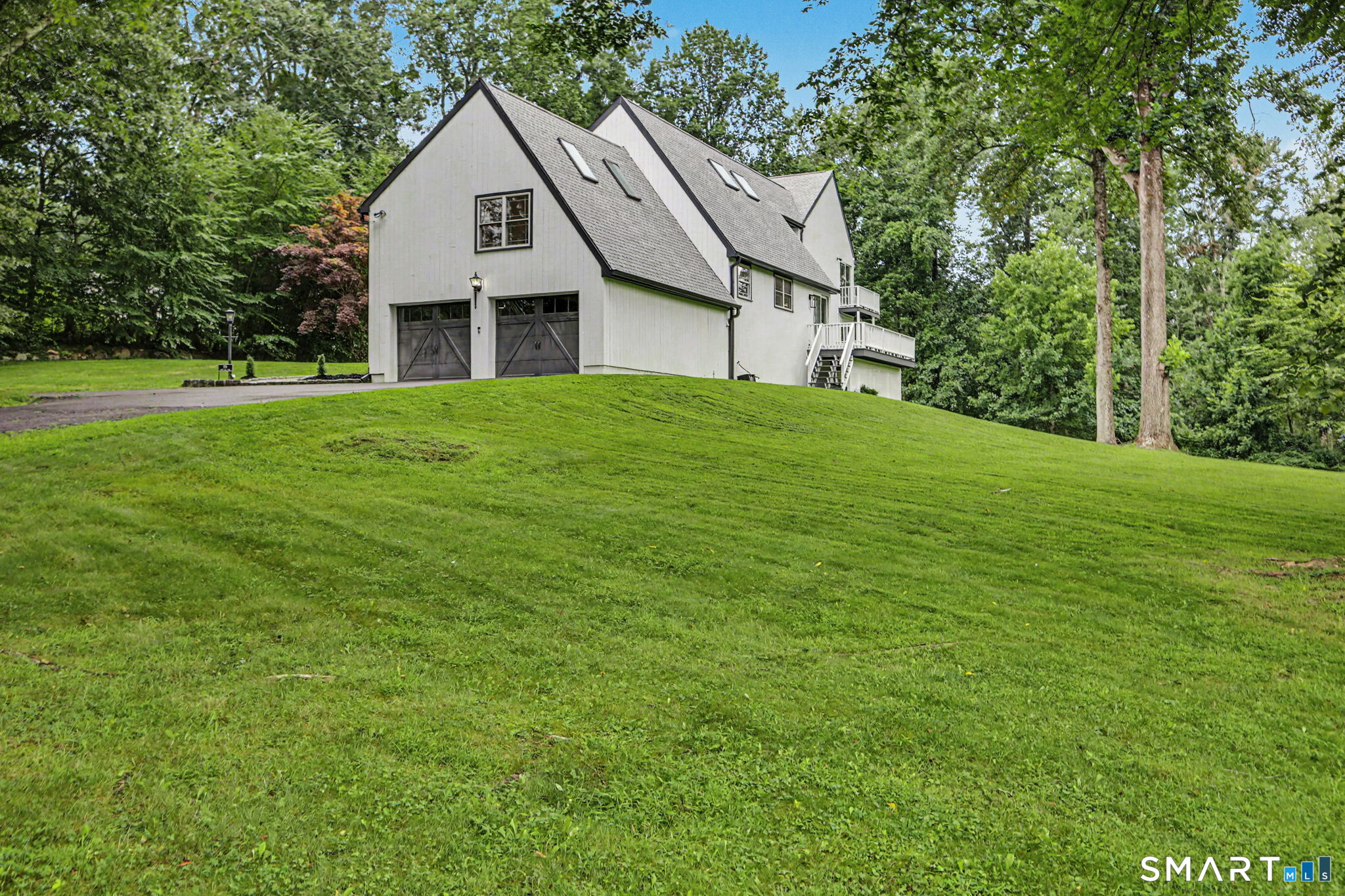 White gabled house with two garage doors and a raised deck above a broad sloping lawn.