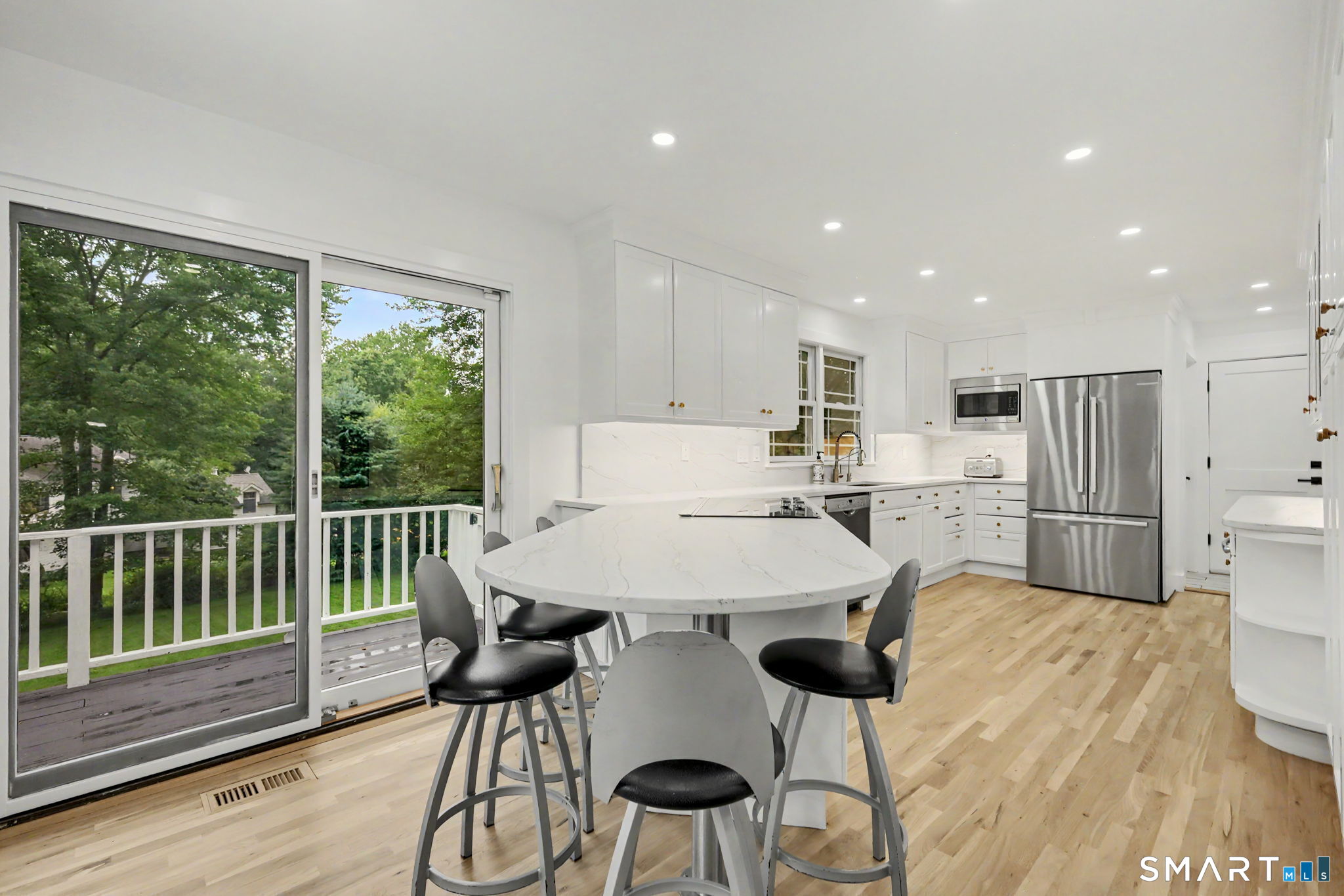 Bright white kitchen with a large island and sliding doors opening onto a tree-lined deck.