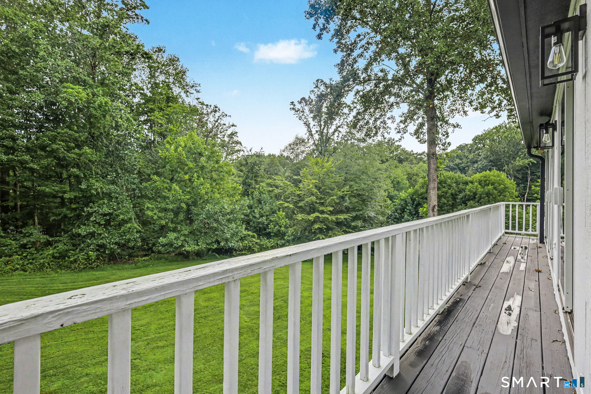 Wooden deck with white railings overlooking a lawn and leafy trees.