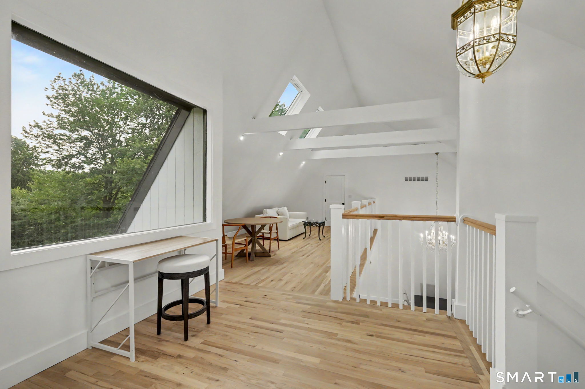 Upper-level landing with a large angled window, skylights, hardwood floors, and a furnished sitting area.