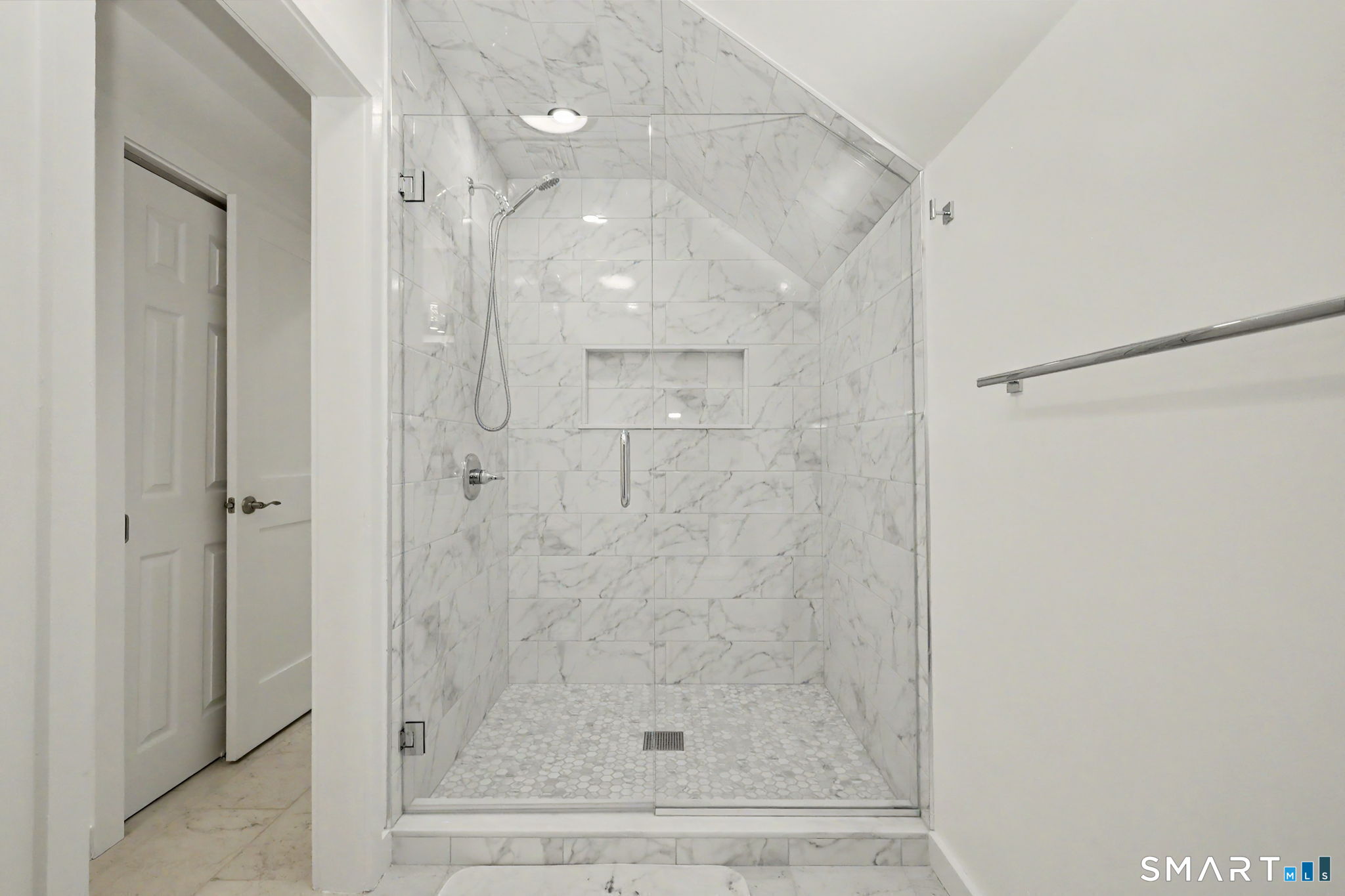 Walk-in shower with marble-look tile, clear glass enclosure, recessed niche, and hexagonal mosaic floor.