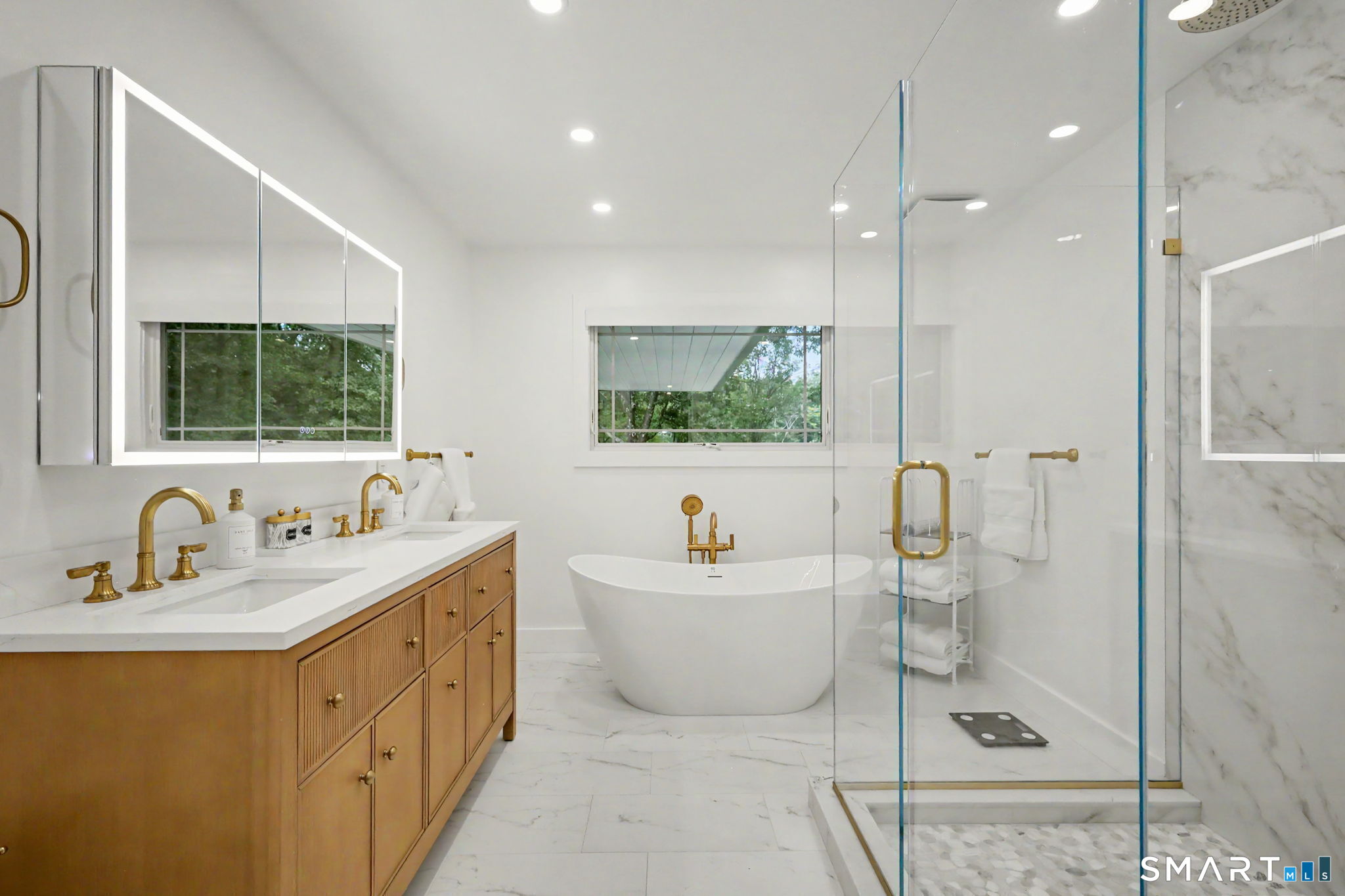 Modern bathroom with a freestanding tub, glass shower, marble-look tile, and wood double vanity.