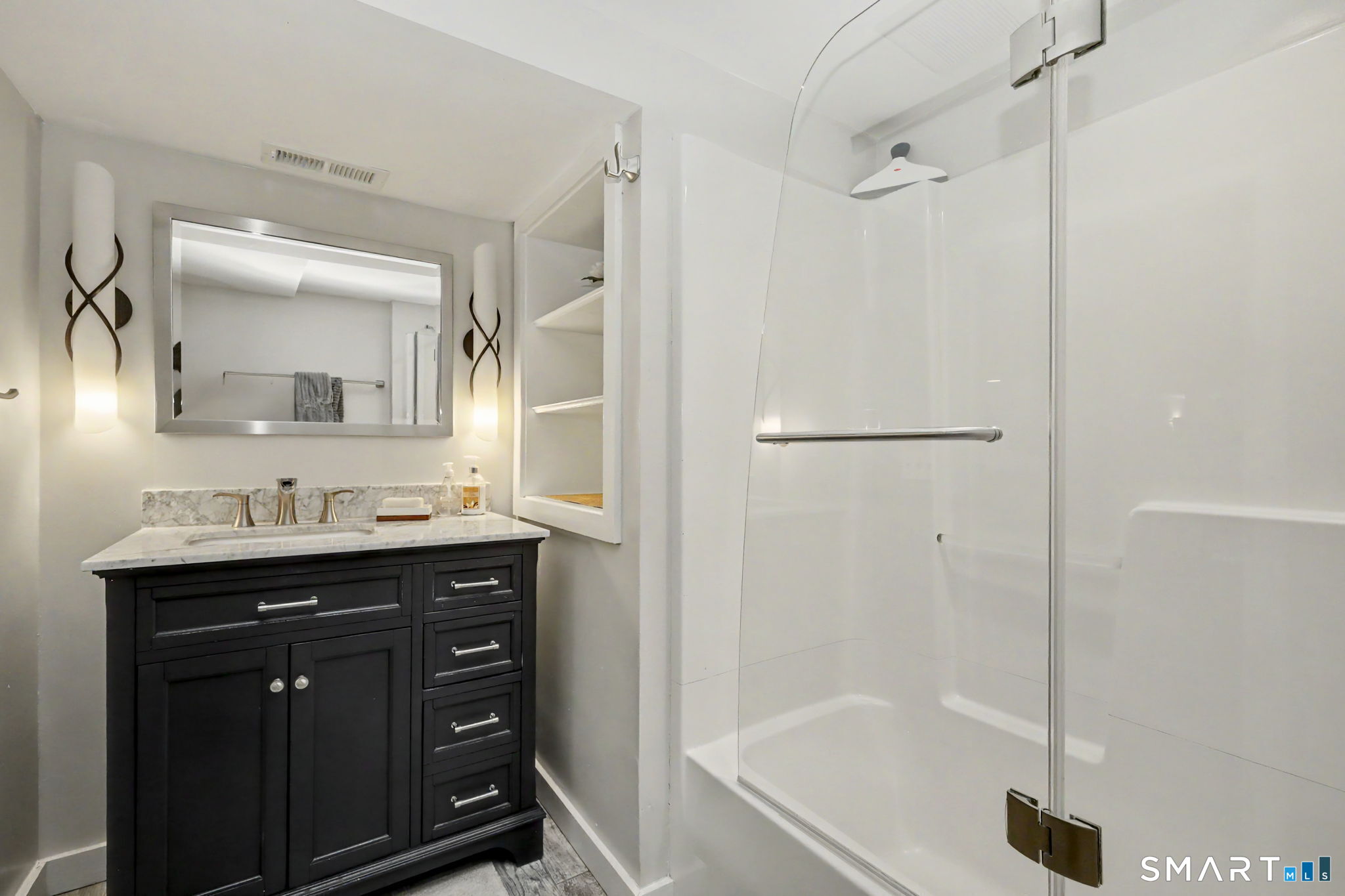 Bathroom with a glass-enclosed shower and dark vanity topped by a marble counter.