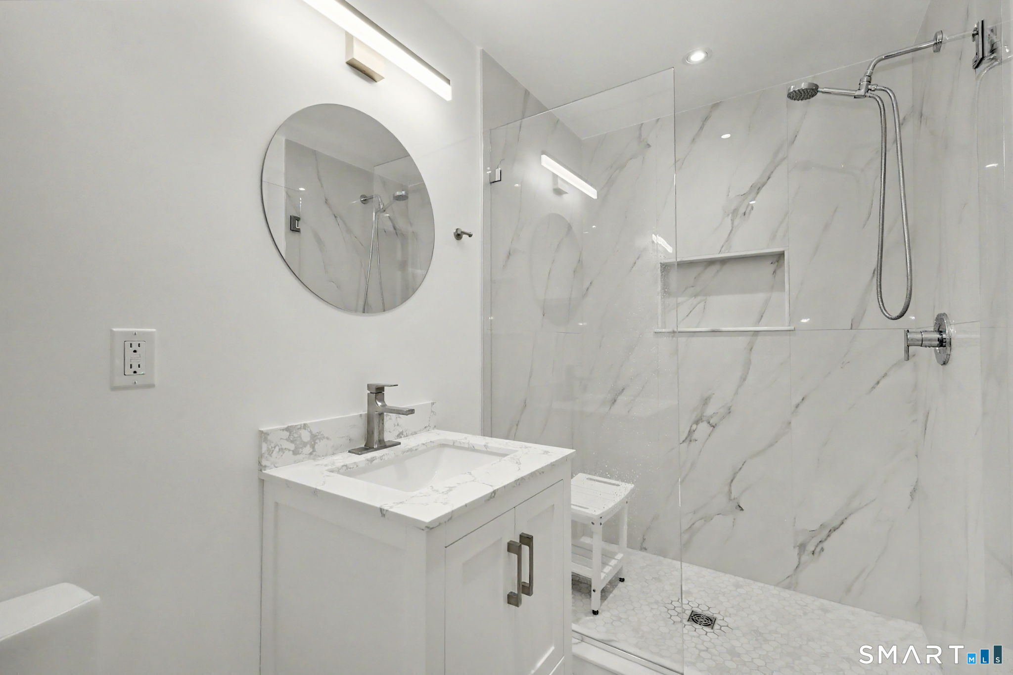 Modern bathroom with a marble vanity, round mirror, and glass-enclosed shower.