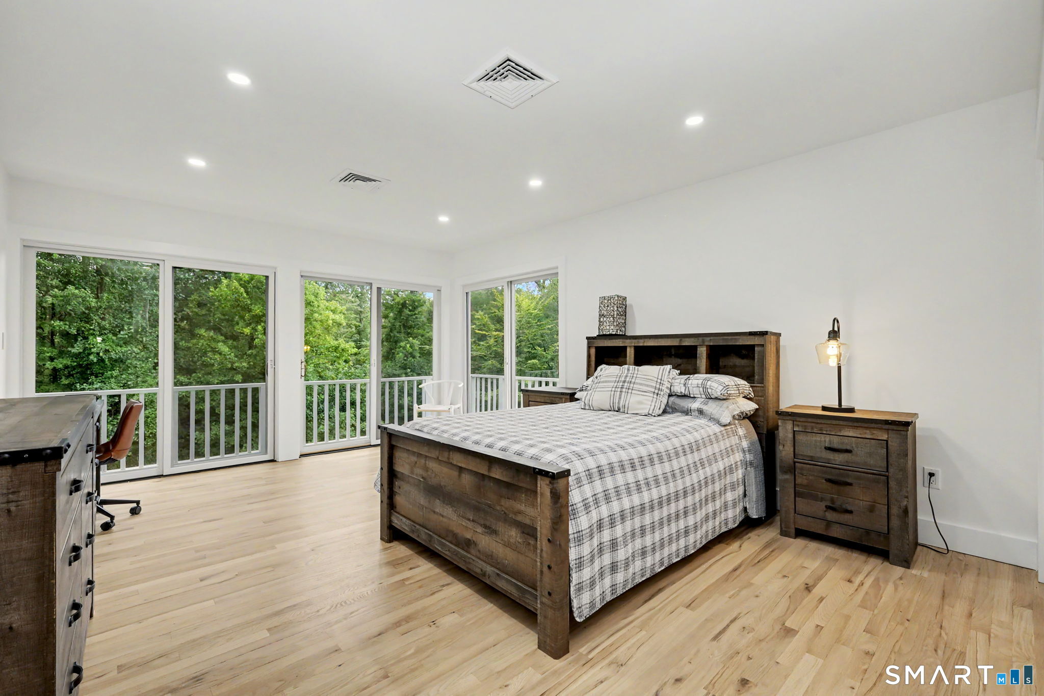 Bedroom with a rustic wood bed, hardwood floors, and wide windows overlooking trees.