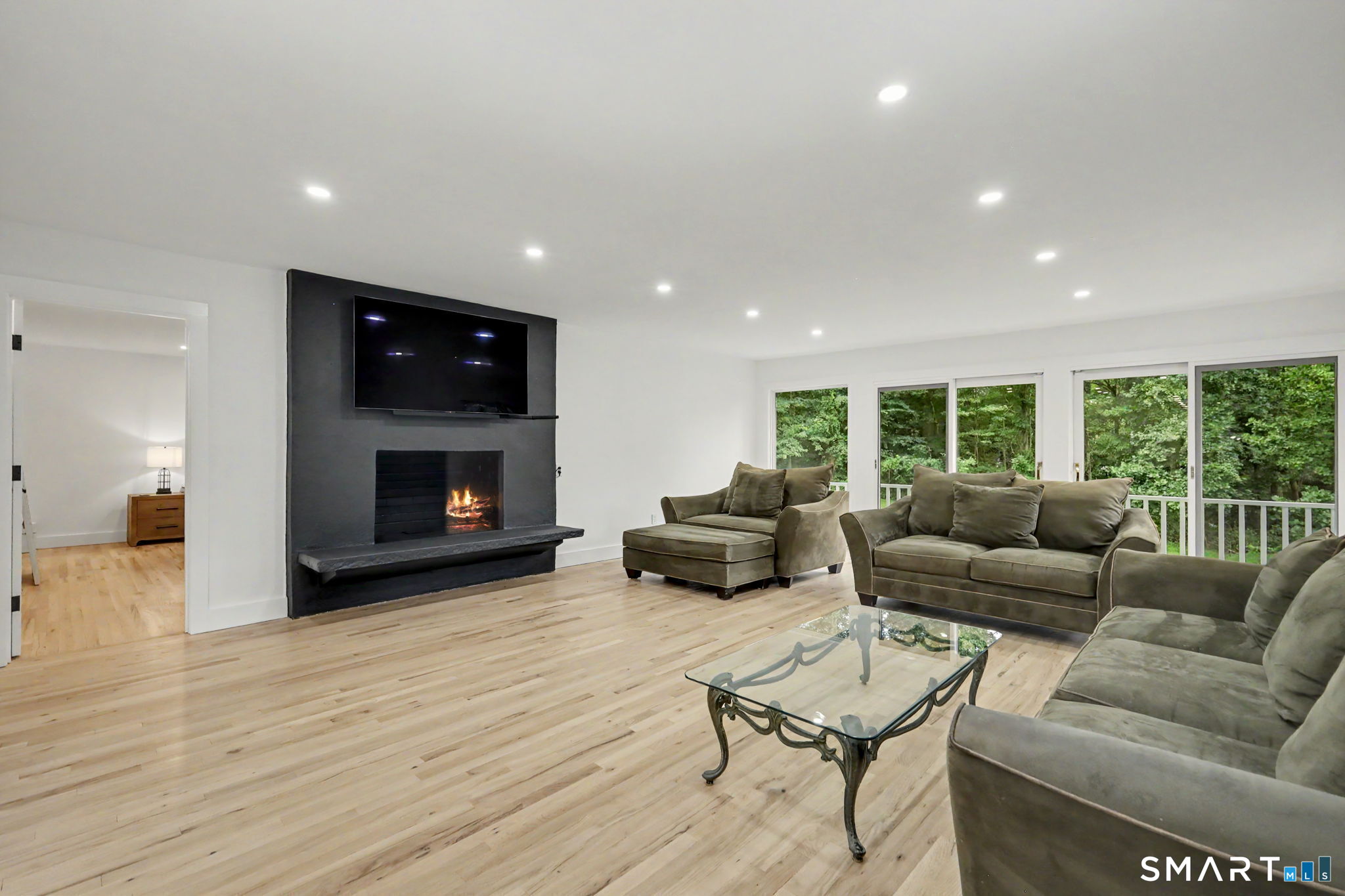 Living room with gray seating, a glass coffee table, and a lit fireplace beneath a wall-mounted television.