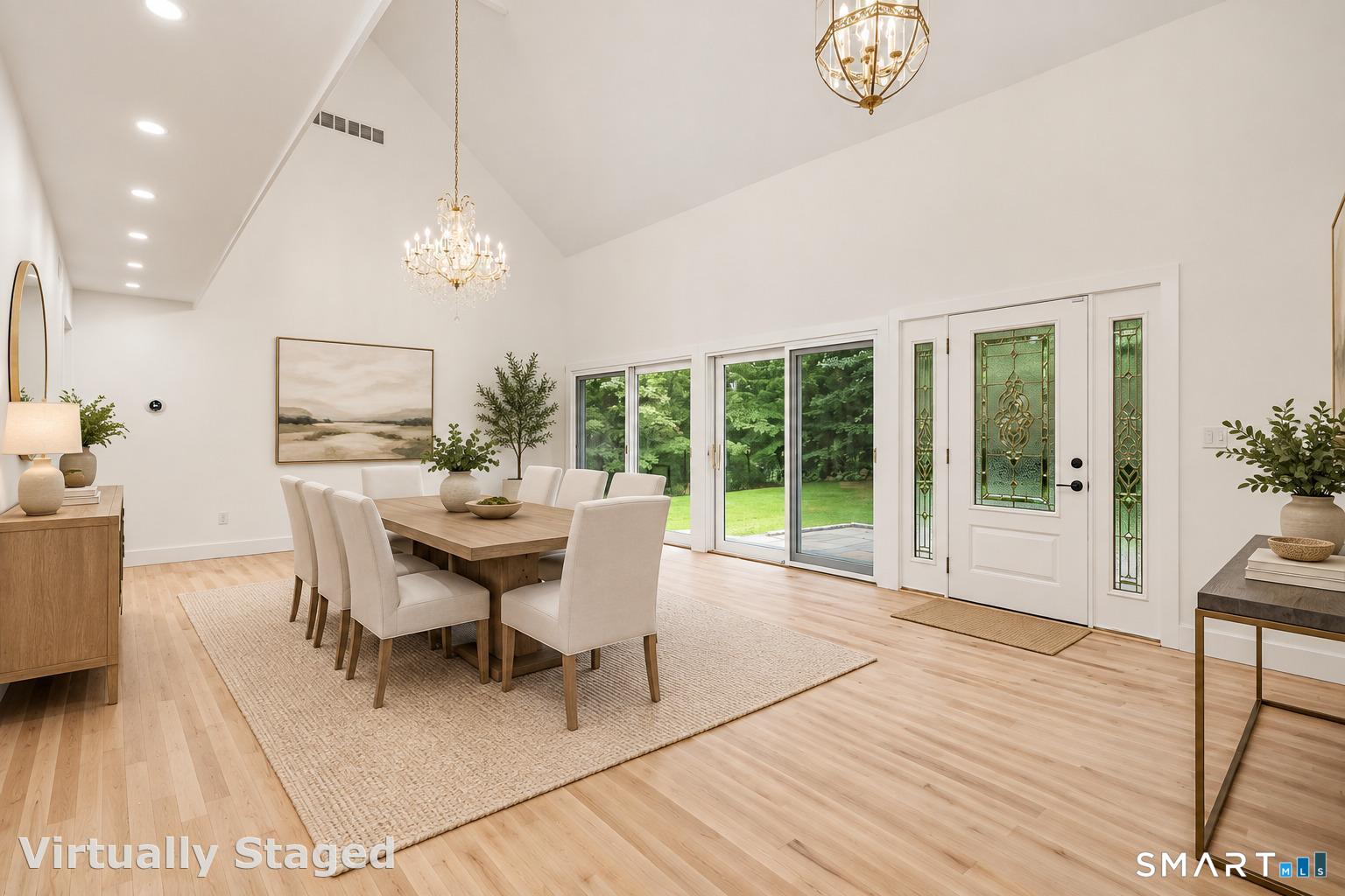 Dining room with a vaulted ceiling, wood table, two chandeliers, and glass doors overlooking the lawn.