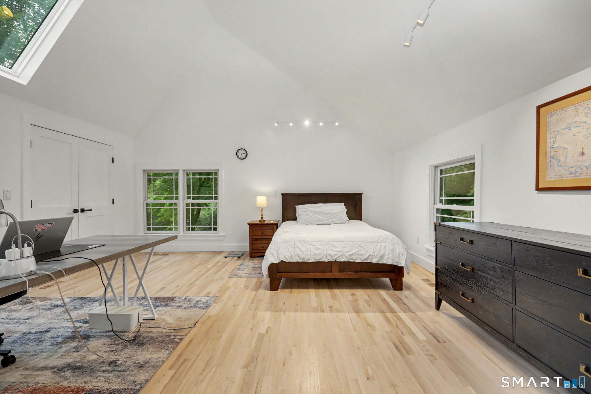 Bedroom with a white bed, vaulted ceiling, skylight, and hardwood floors.