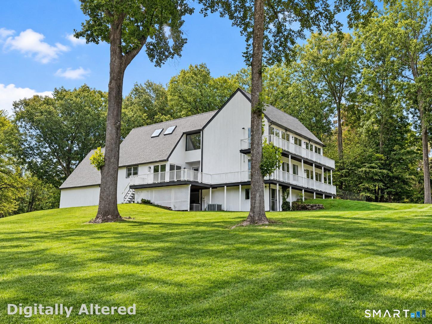 White multi-level house with long balconies on a tree-shaded lawn.