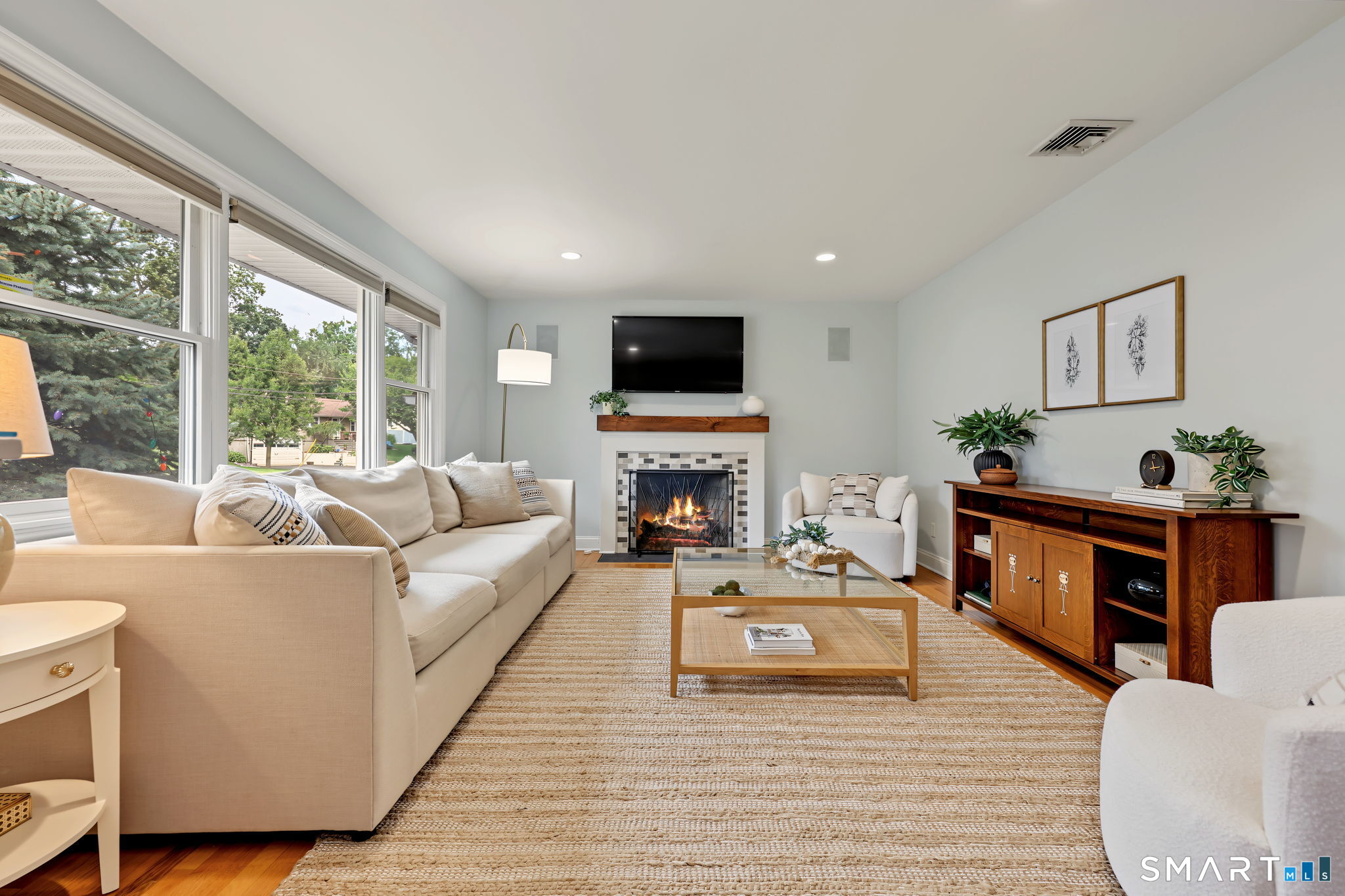 Furnished living room with a beige sectional, large windows, and a lit fireplace.