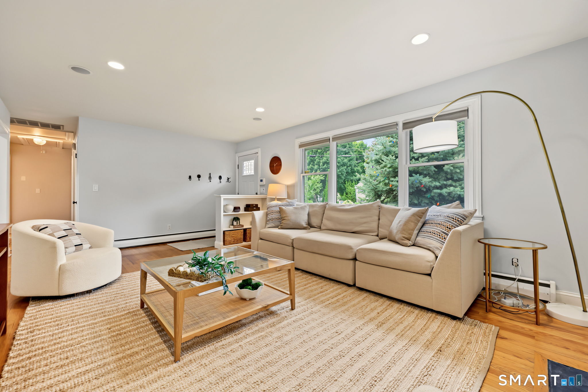 Living room with a beige sectional, large windows overlooking greenery, and a glass-topped coffee table.