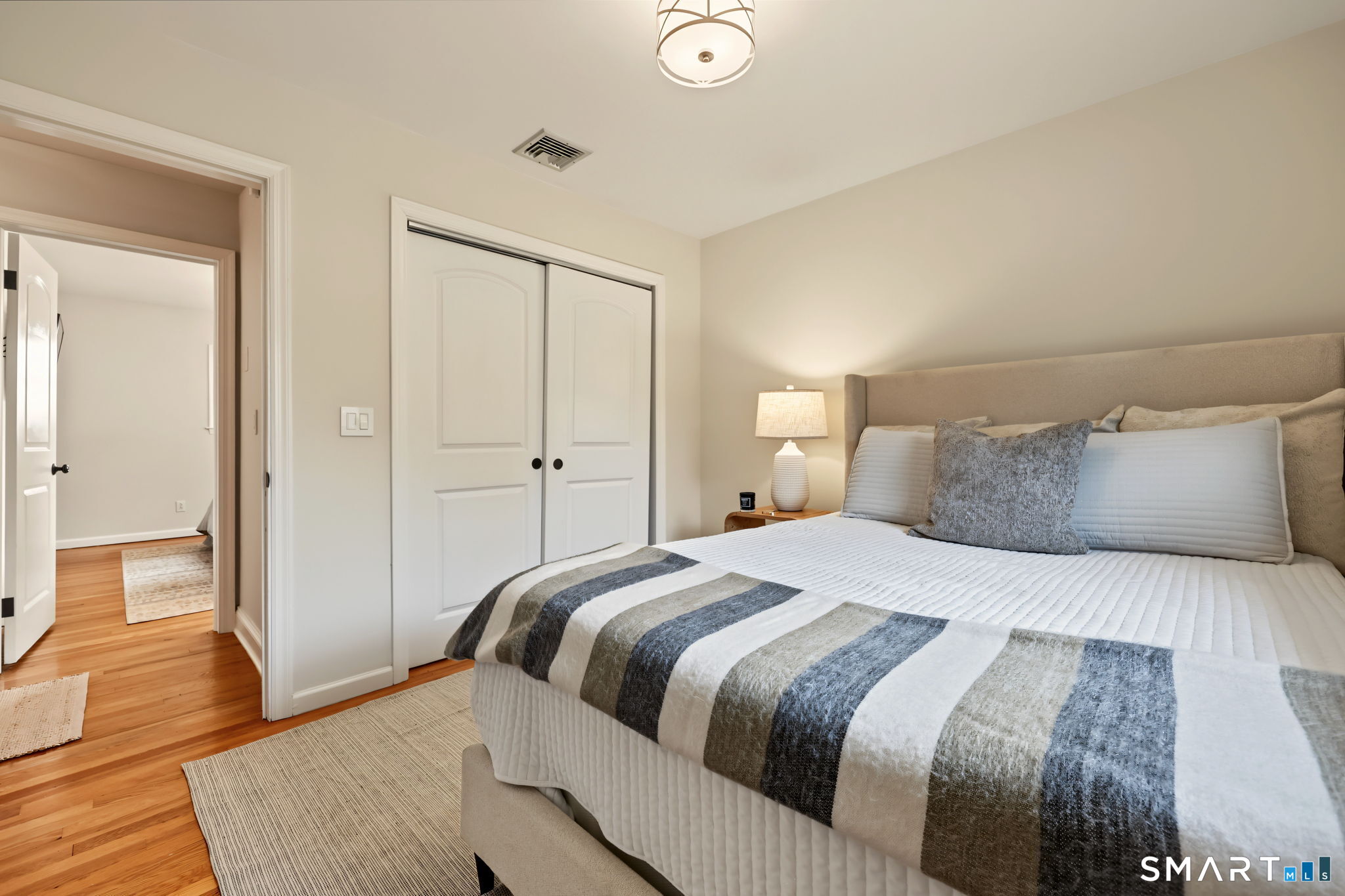 Furnished bedroom with a large bed, gray striped throw, white closet doors, and hardwood floors.